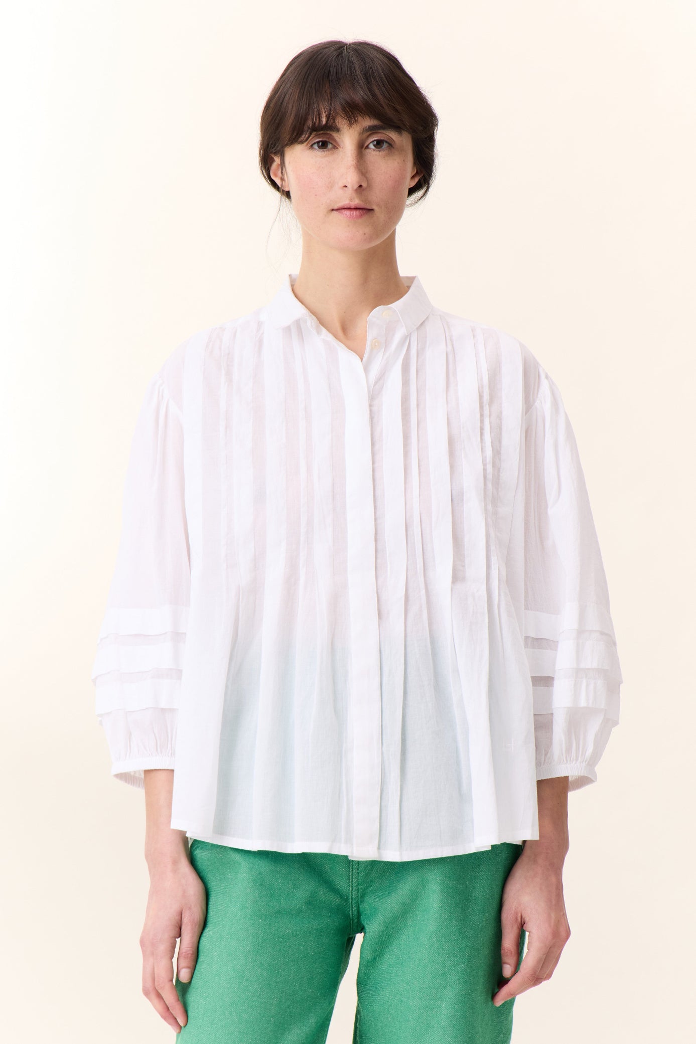 Model wearing white short sleeve shirt with frill detail on a white background paired with green pants