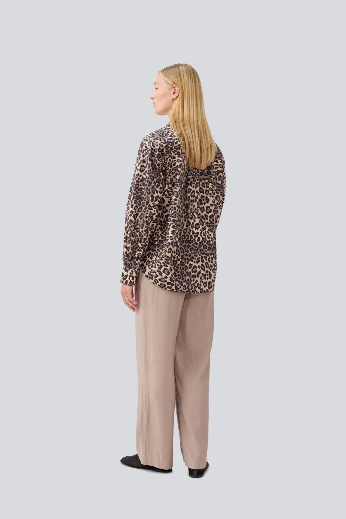 Woman wearing a leopard print blouse and beige pants on a light gray background