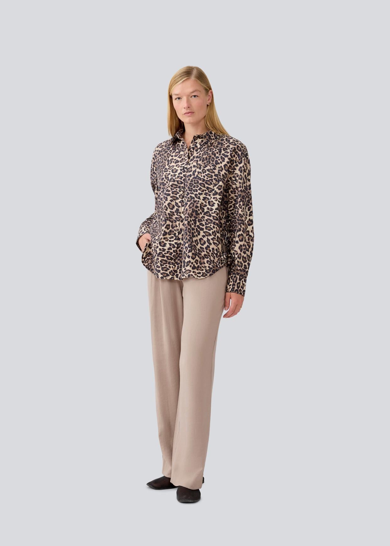 Woman wearing a leopard print blouse and beige pants on a light gray background