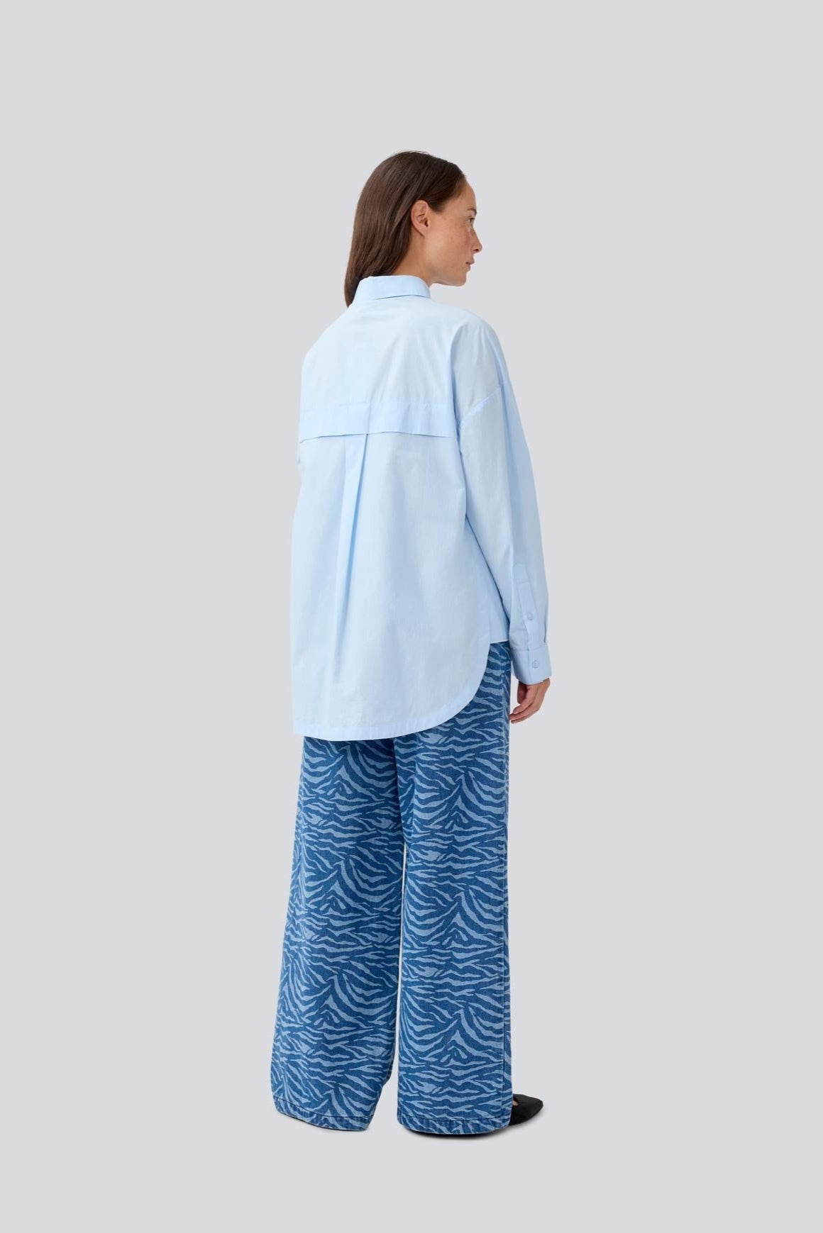Woman wearing a light blue shirt and blue patterned pants on a white background