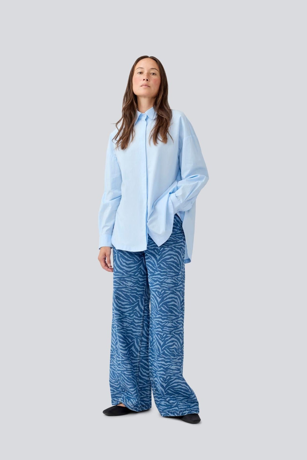 Model wearing a light blue shirt and blue zebra patterned pants on a white background