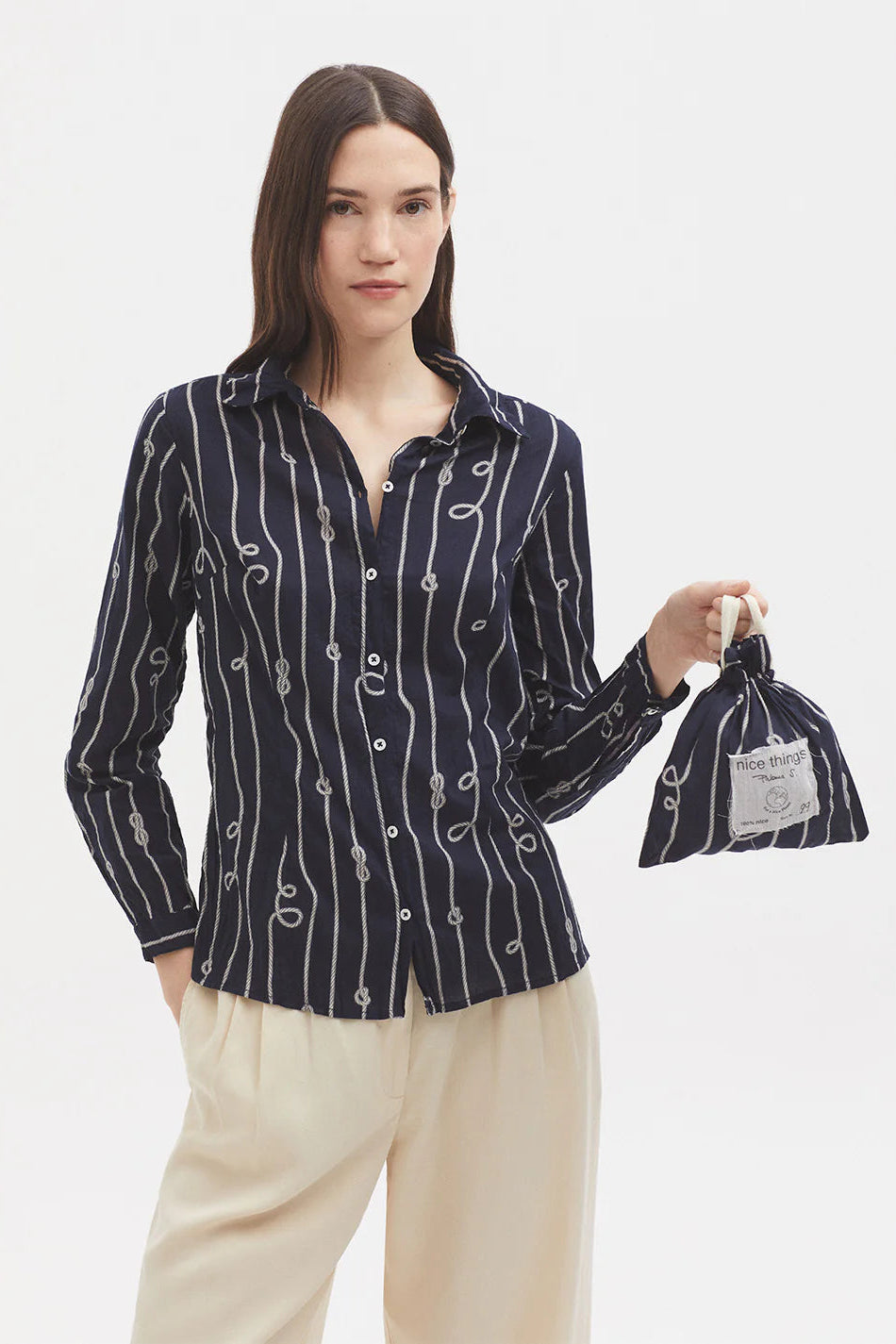 Woman wearing a dark blue patterned shirt and beige pants, holding a black bag with a brand label.