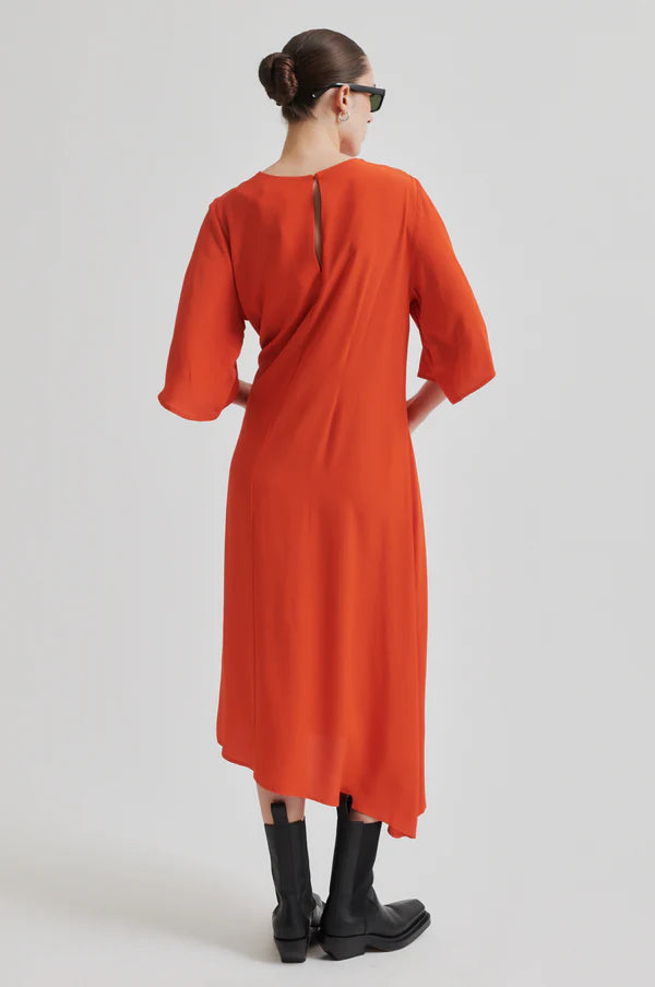 Model wearing orange short sleeve midi dress with asymmetrical hem and tie waist. Wearing black boots and sunglasses.