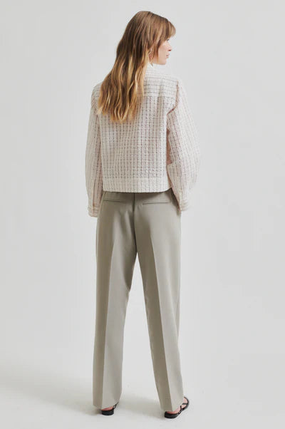 Model wearing a light checkered longs leeve seersucker blouse and beige pants on a white background