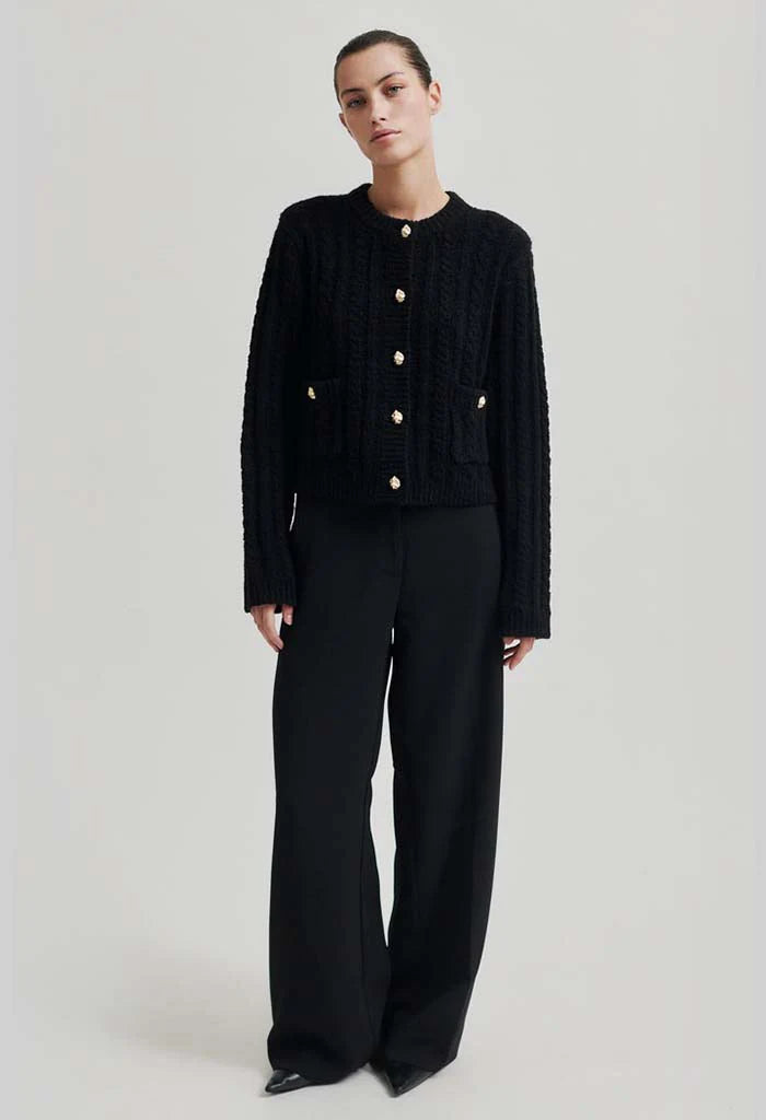 Black mock neck cardigan with gold button detail down front and on two front pockets at hip height.