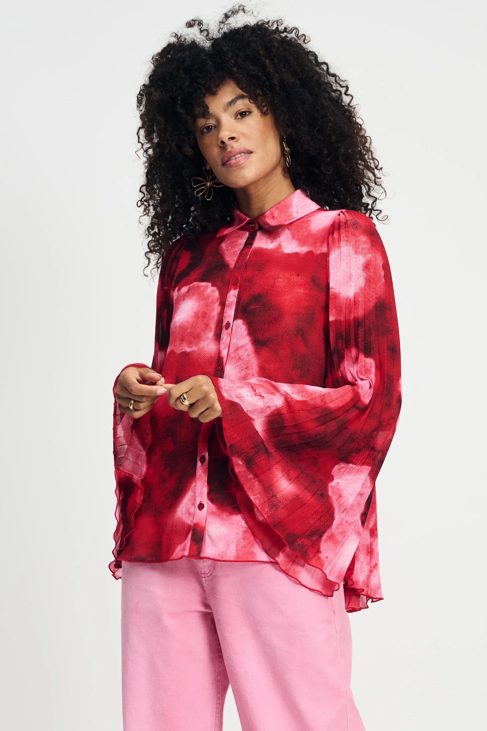 Model wearing long sleeve red and pink floral shirt with wide sleeves and pink pants on a plain background.