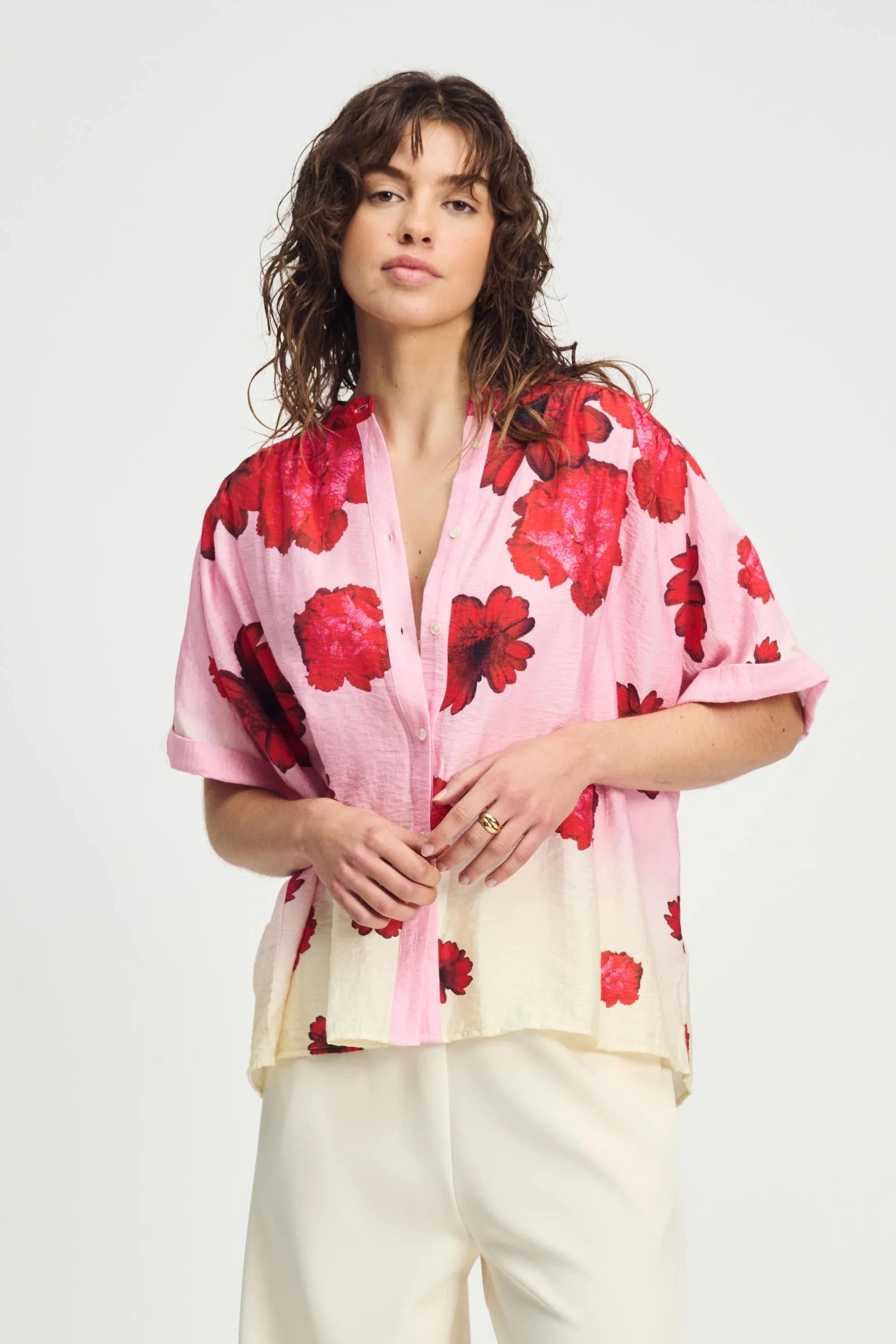 Woman wearing a pink floral short sleeve blouse and cream pants on a white background