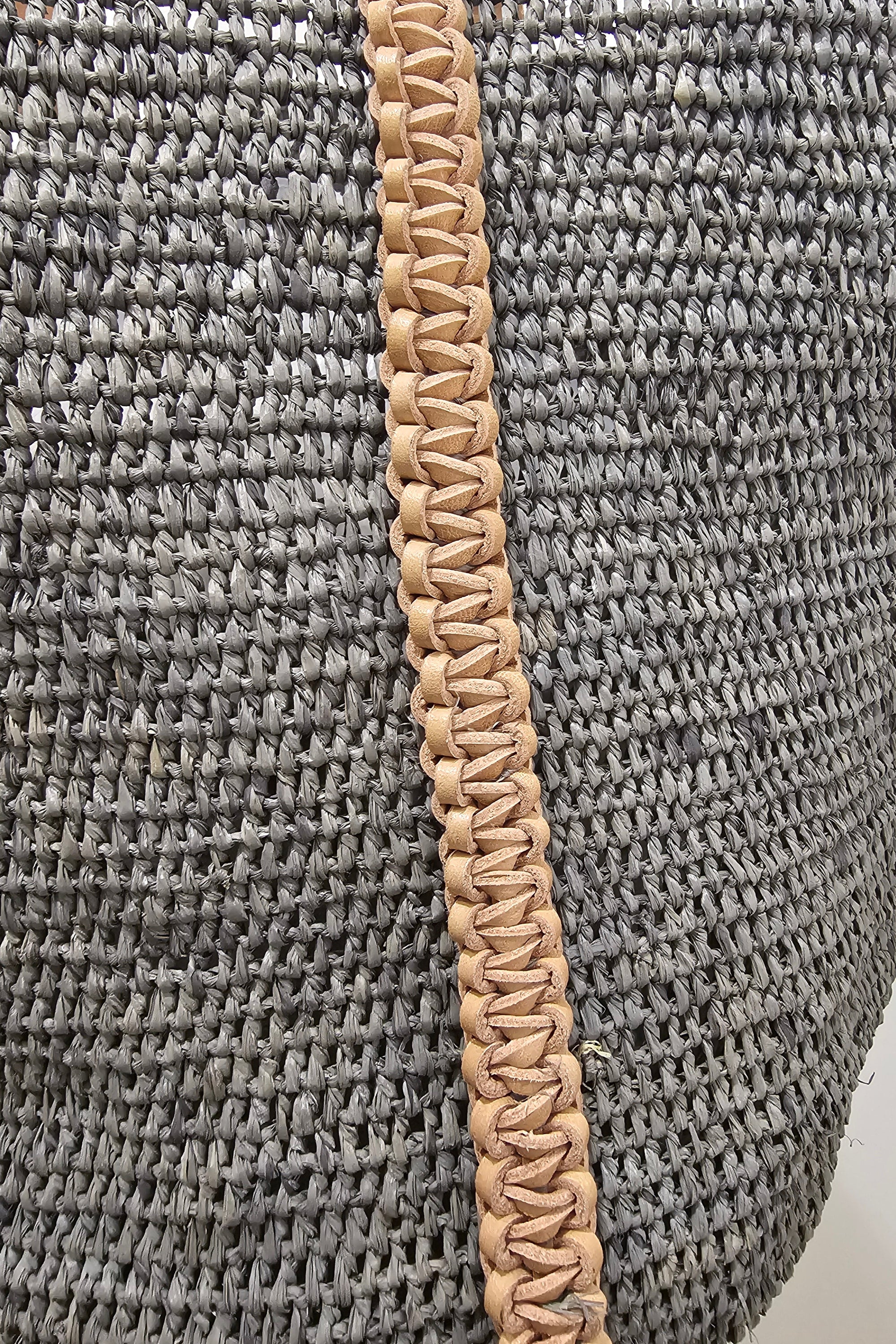 Woven handbag with brown leather trim on a white background