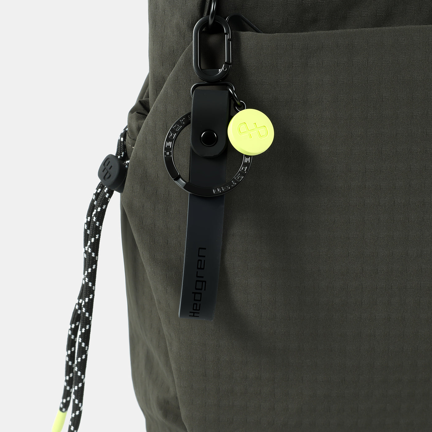 Close-up of a dark olive green cross body bag with a black strap and yellow tag on a white background