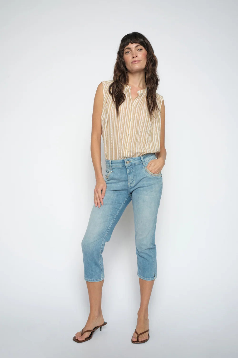 Woman wearing a beige sleeveless top and light blue jeans on a white background