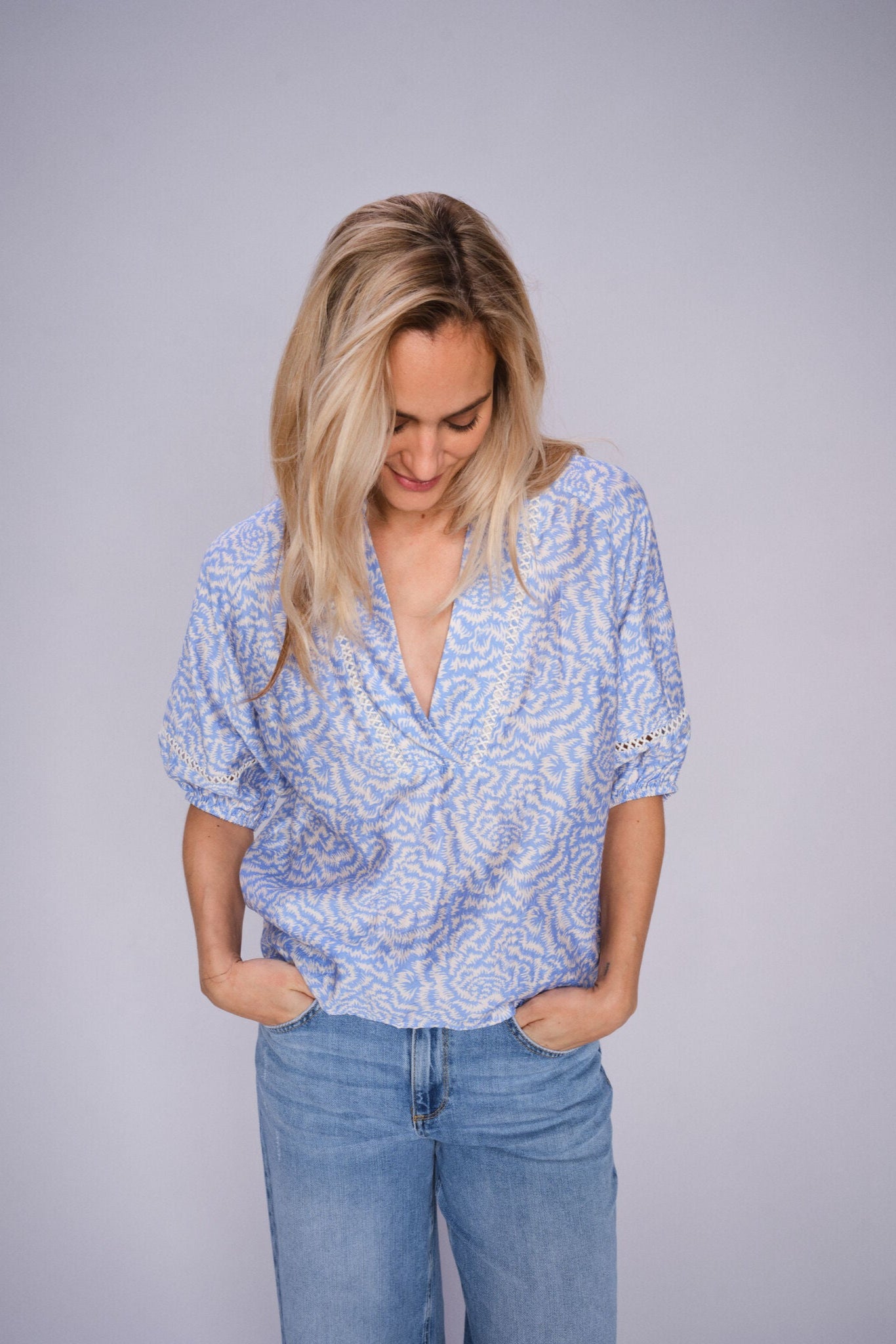 Woman wearing a blue patterned blouse and light blue jeans on a gray background
