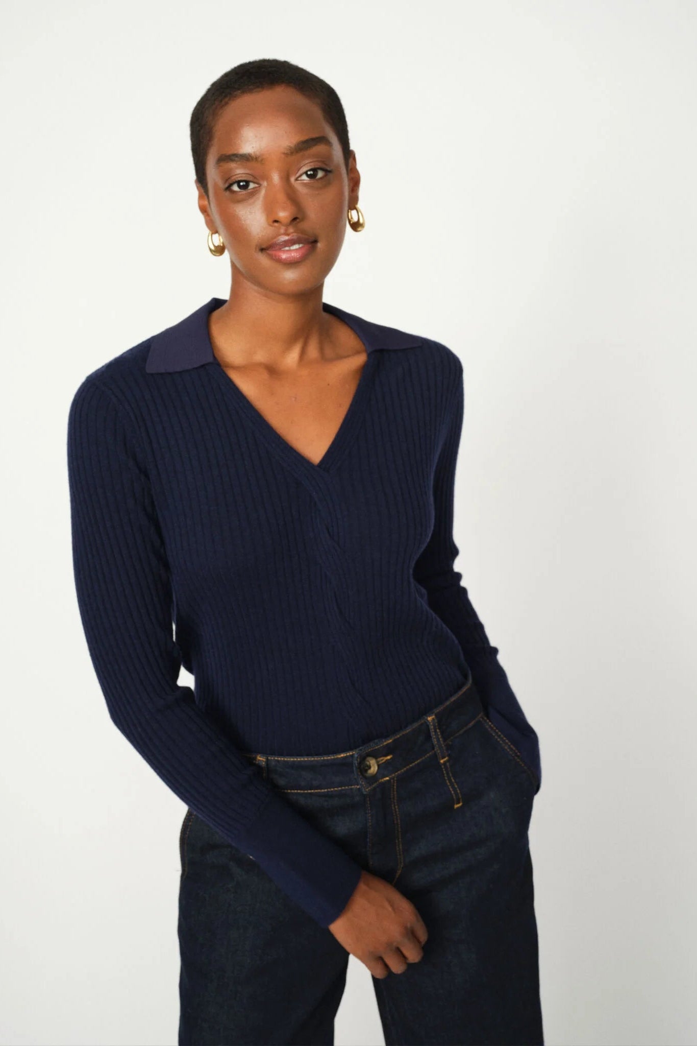 Woman wearing a navy blue polo ribbed sweater and jeans on a white background