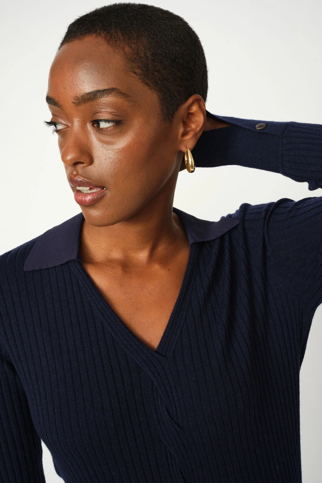 Woman wearing a navy blue polo ribbed sweater against a white background