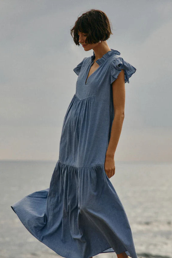 Woman wearing a blue dress with ruffle sleeve standing by a body of water 
