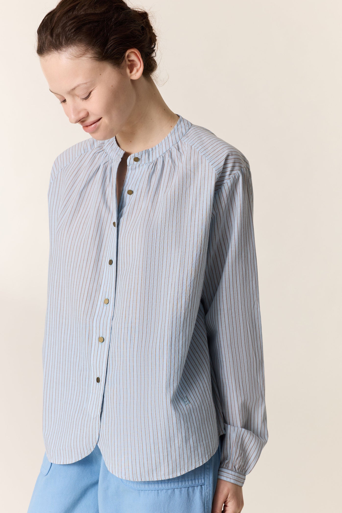 Women shown up close wearing a. blue stripe shirt and blue pants on a plain background. 