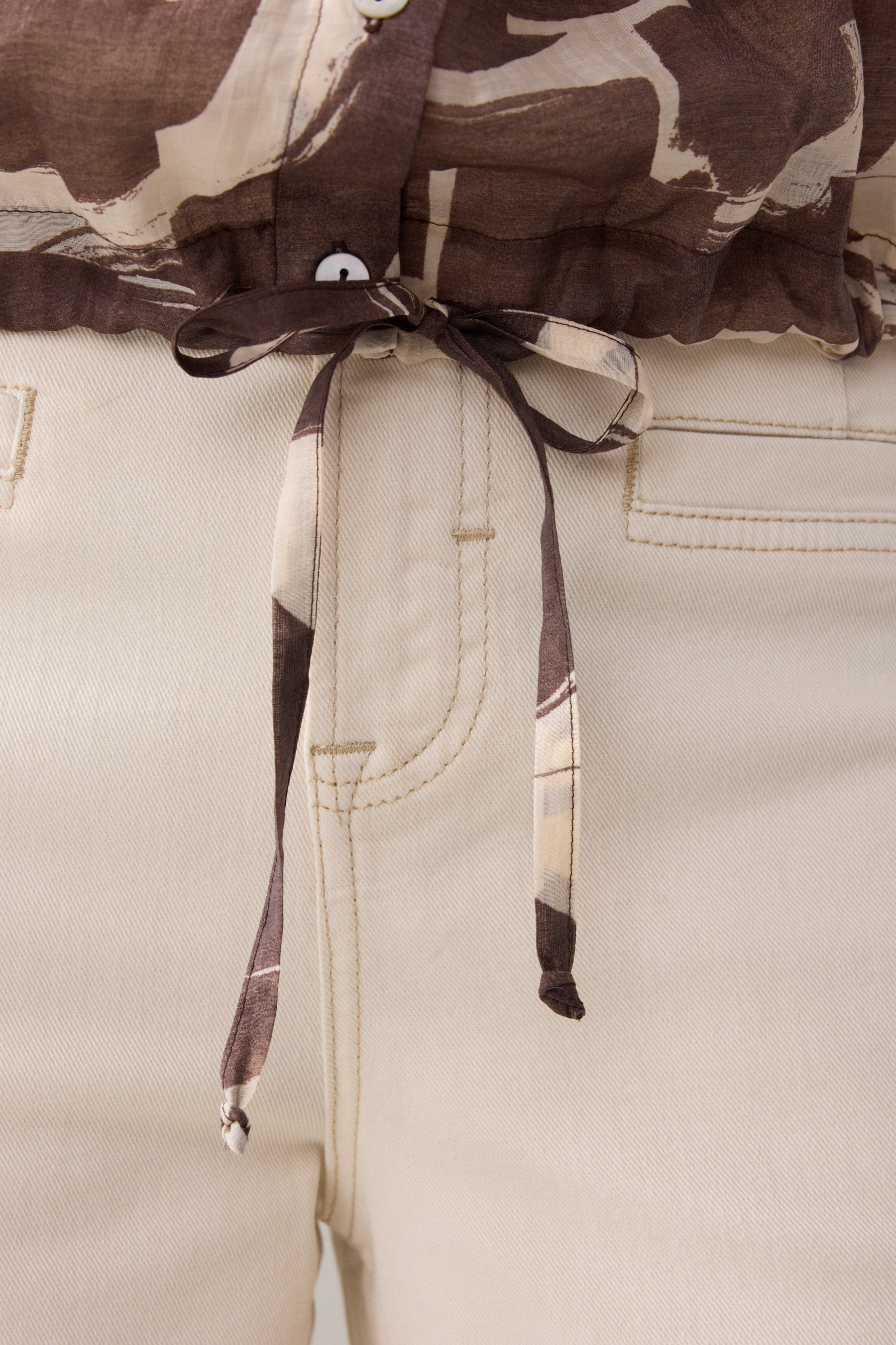 Close up of a brown and cream patterned shirt and cream pants  on a plain background. 