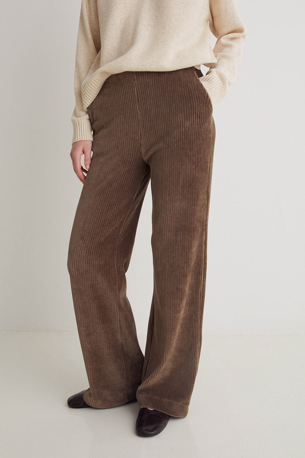 Brown corduroy pants worn by a person on a white background