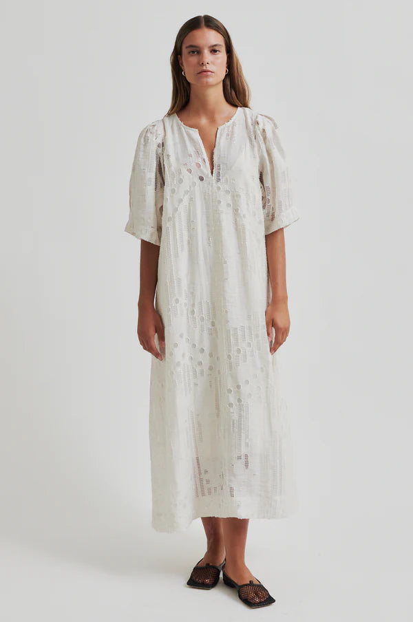 Woman wearing a long off white dress with embroidery detail with short sleeves