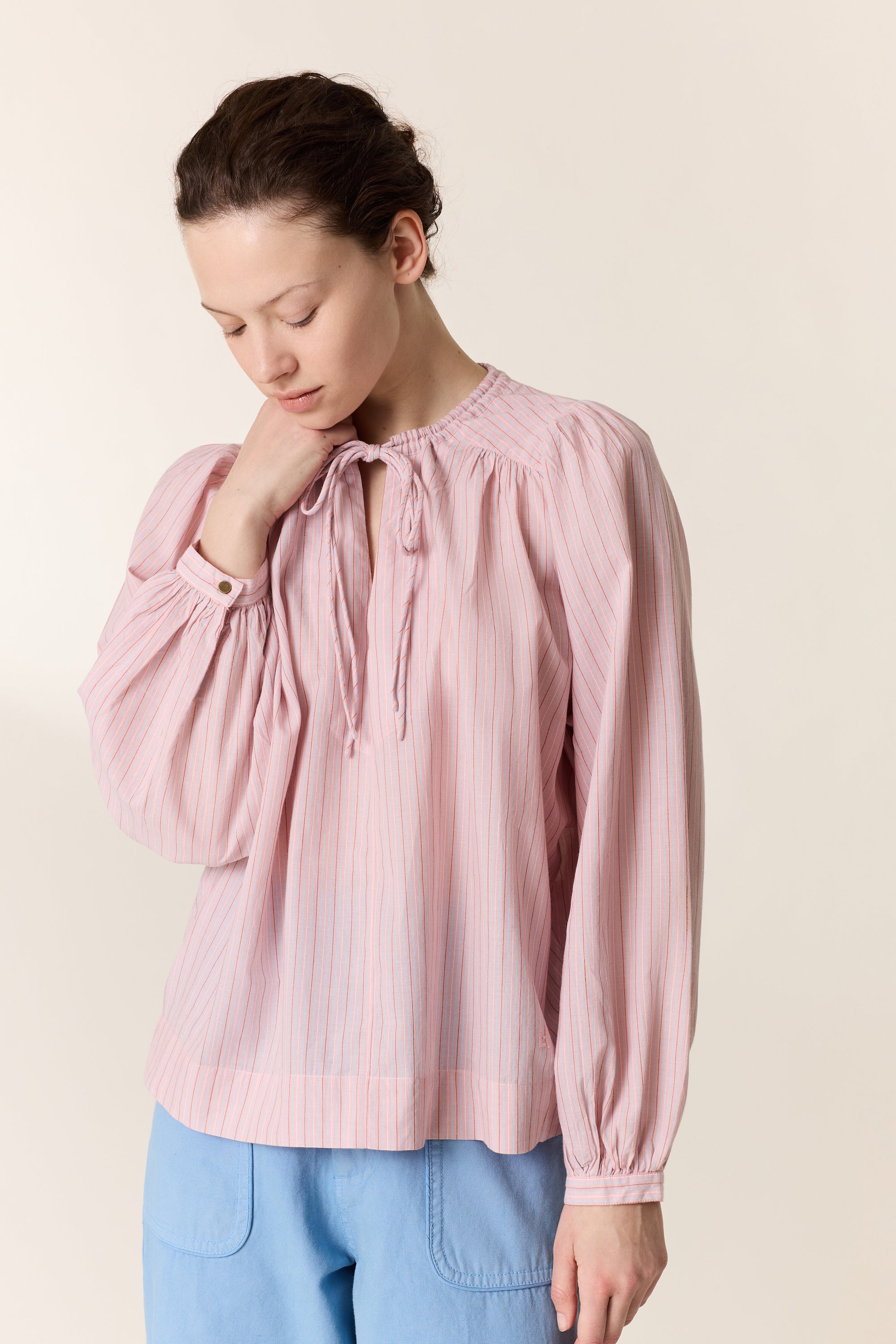 Close up of a woman wearing a pink stripe shirt on a plain background. 
