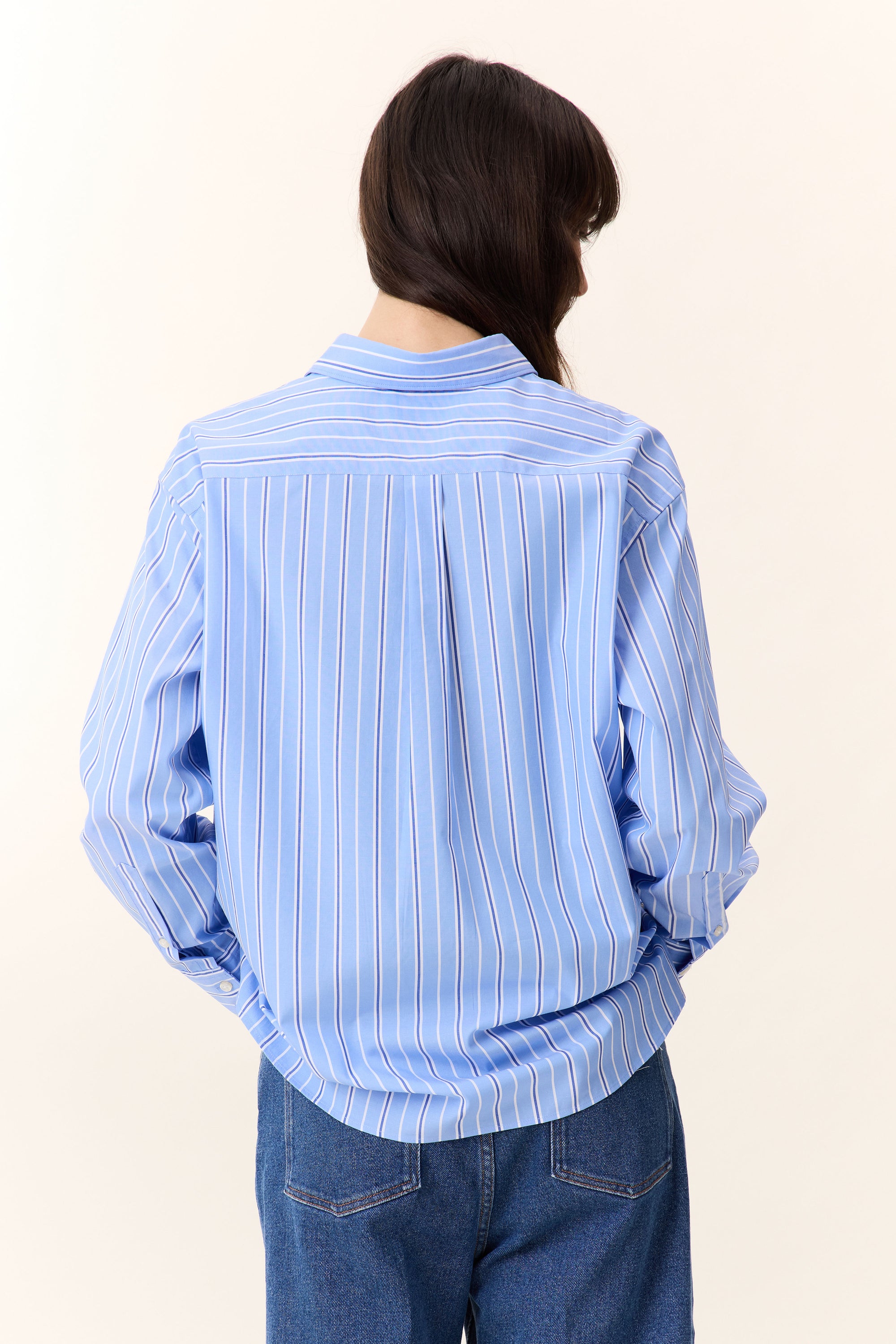 Woman wearing a light blue striped shirt and blue jeans on a white background