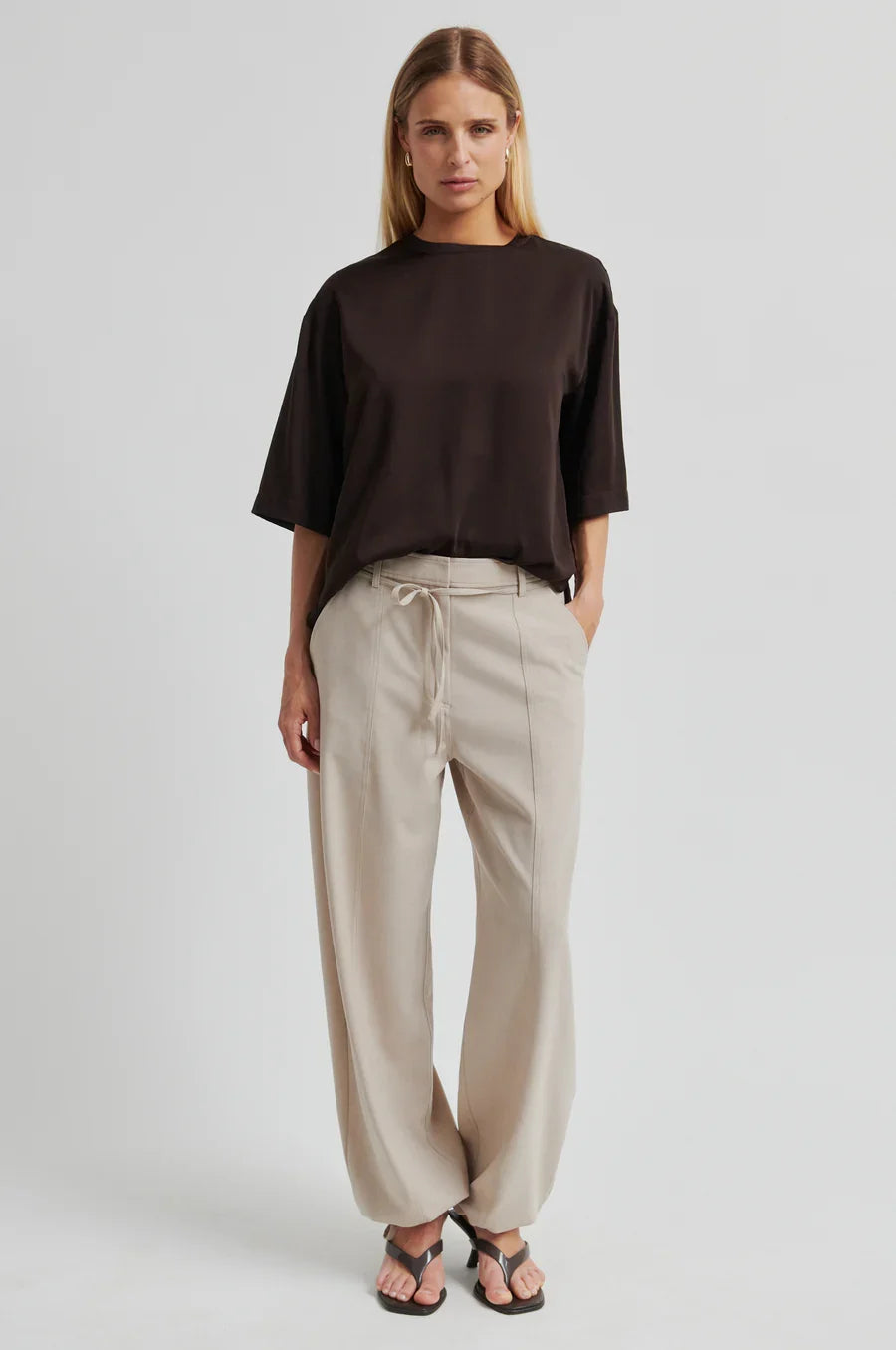 Women wearing a brown oversized shirt and beige pants on a light background