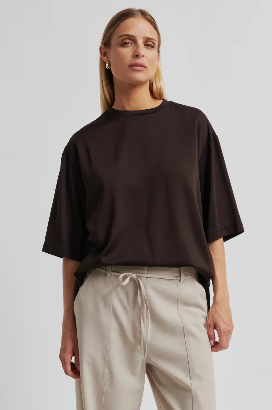Women wearing a brown oversized shirt and beige pants on a light background