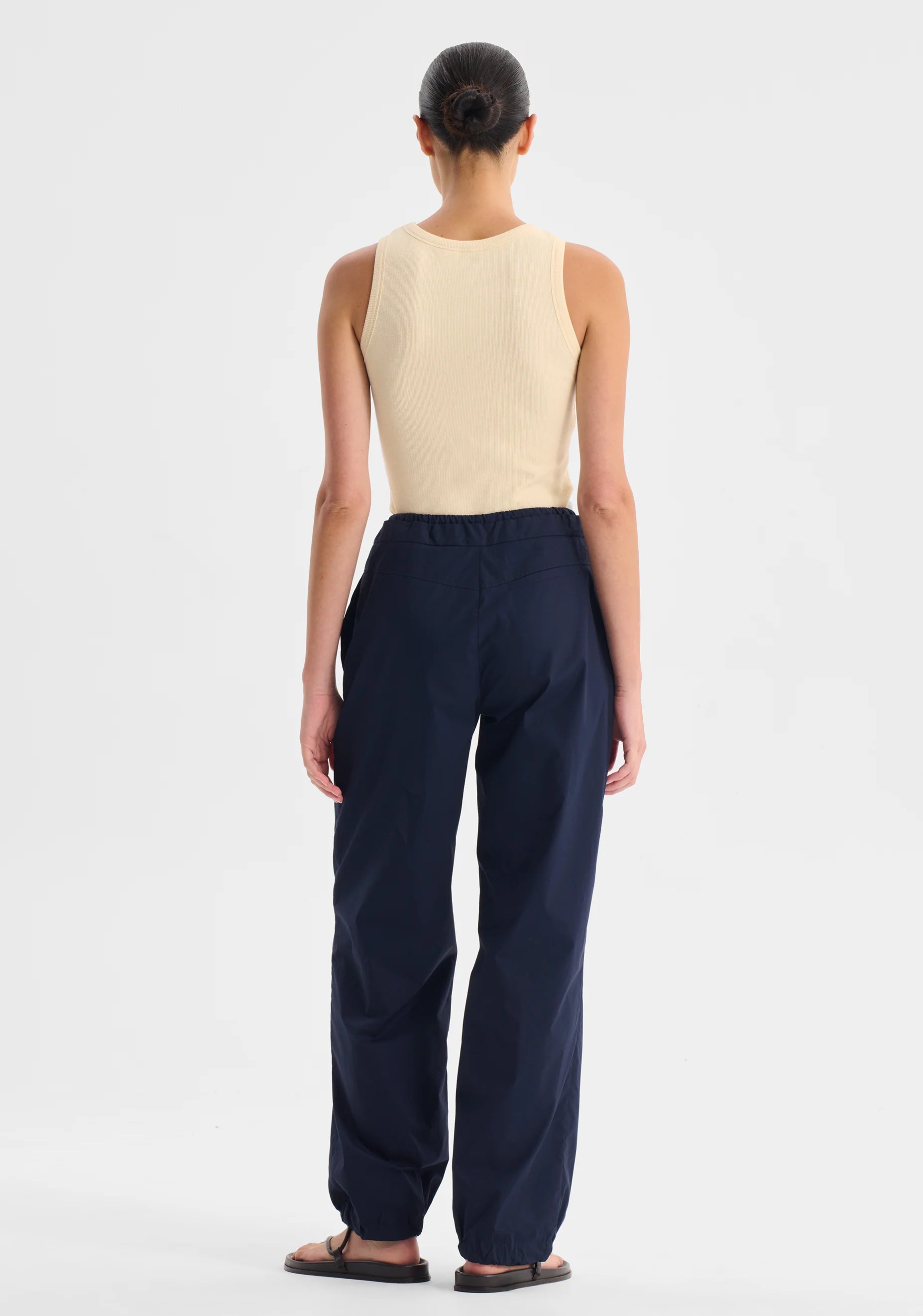 Woman wearing a cream singlet top and navy pants on a white background