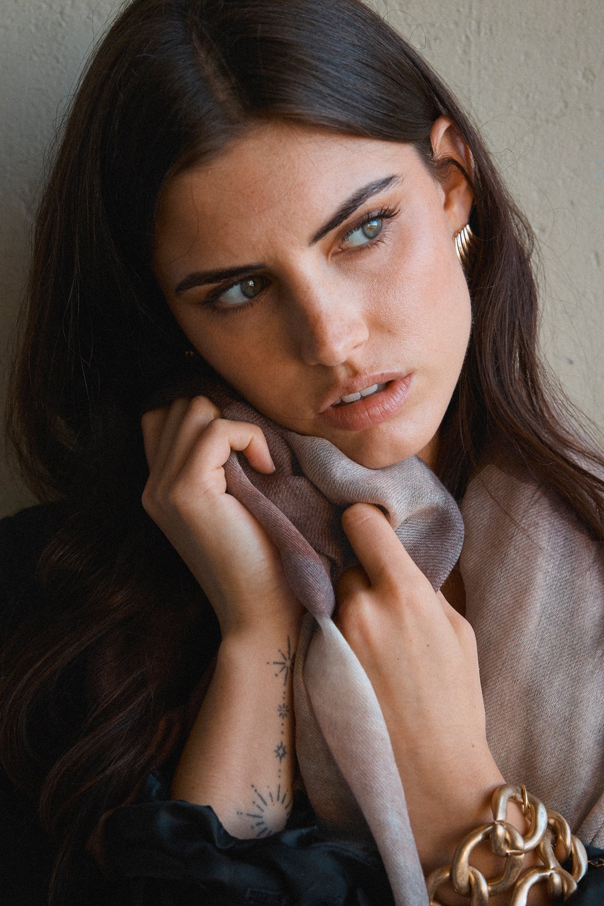 Woman wearing a beige scarf and gold jewelry against a neutral background