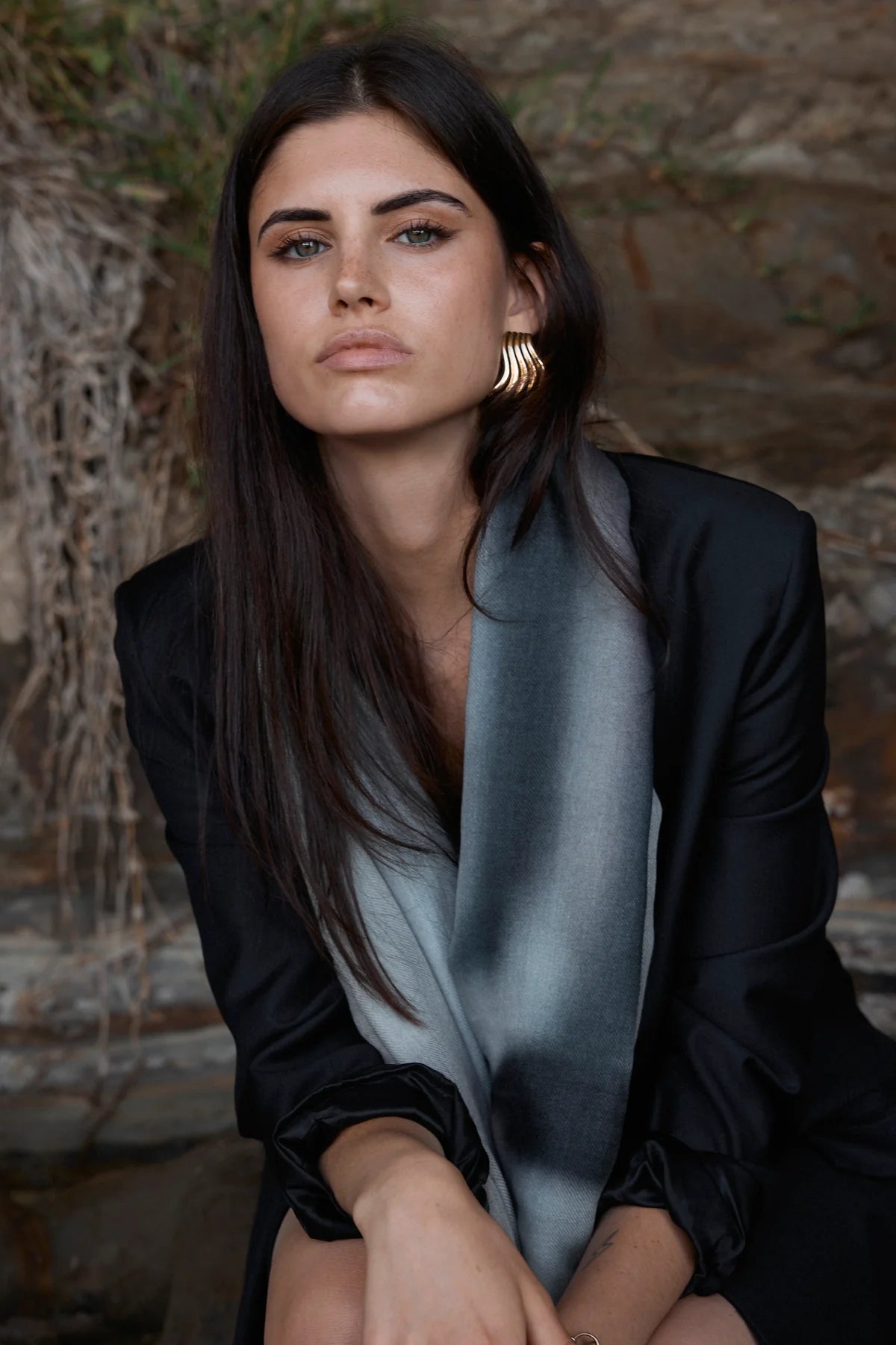 Woman wearing a black outfit with a light blue scarf against a stone wall background