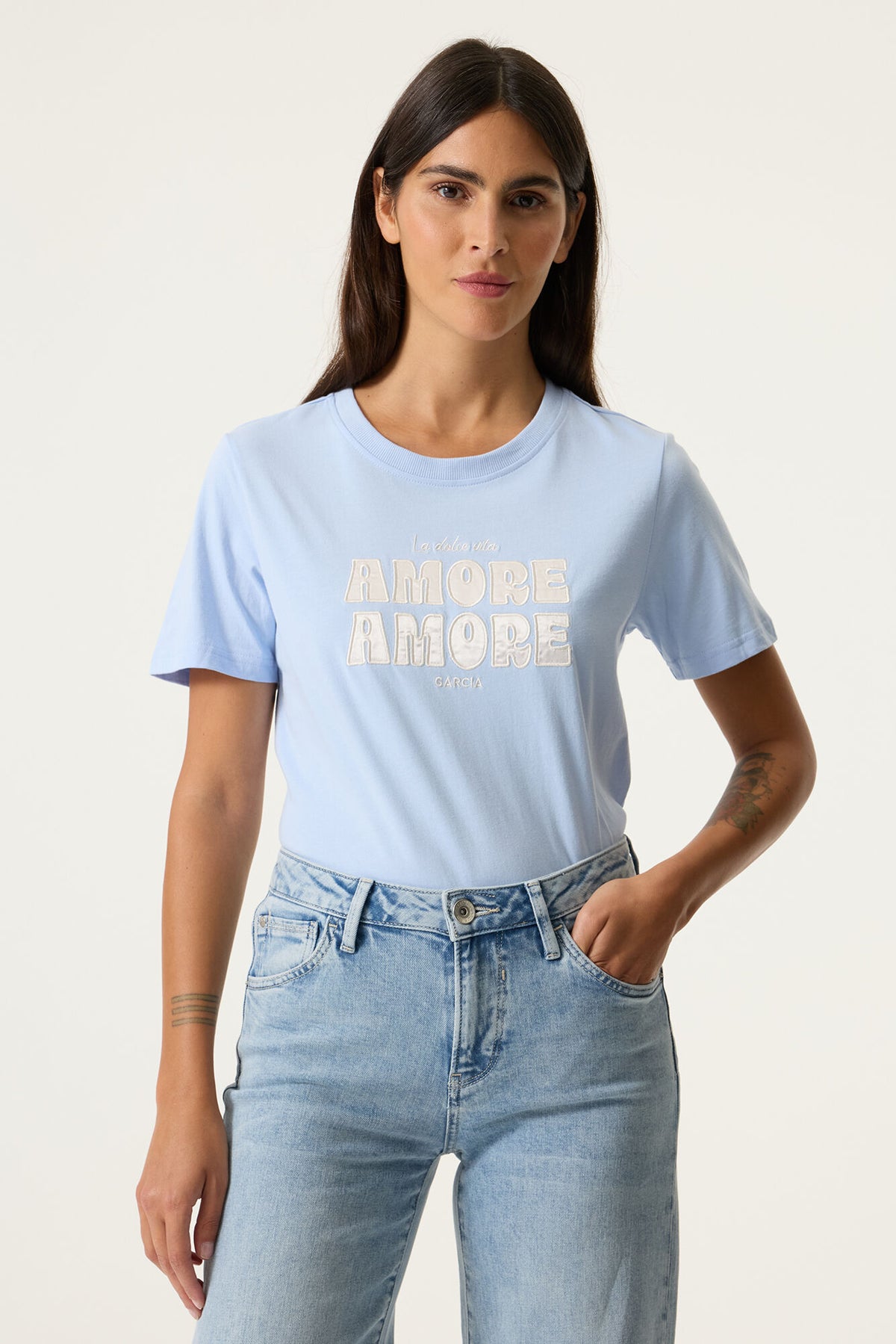 Woman wearing a light blue t-shirt with 'AMORE AMORE' text and light blue jeans on a white background
