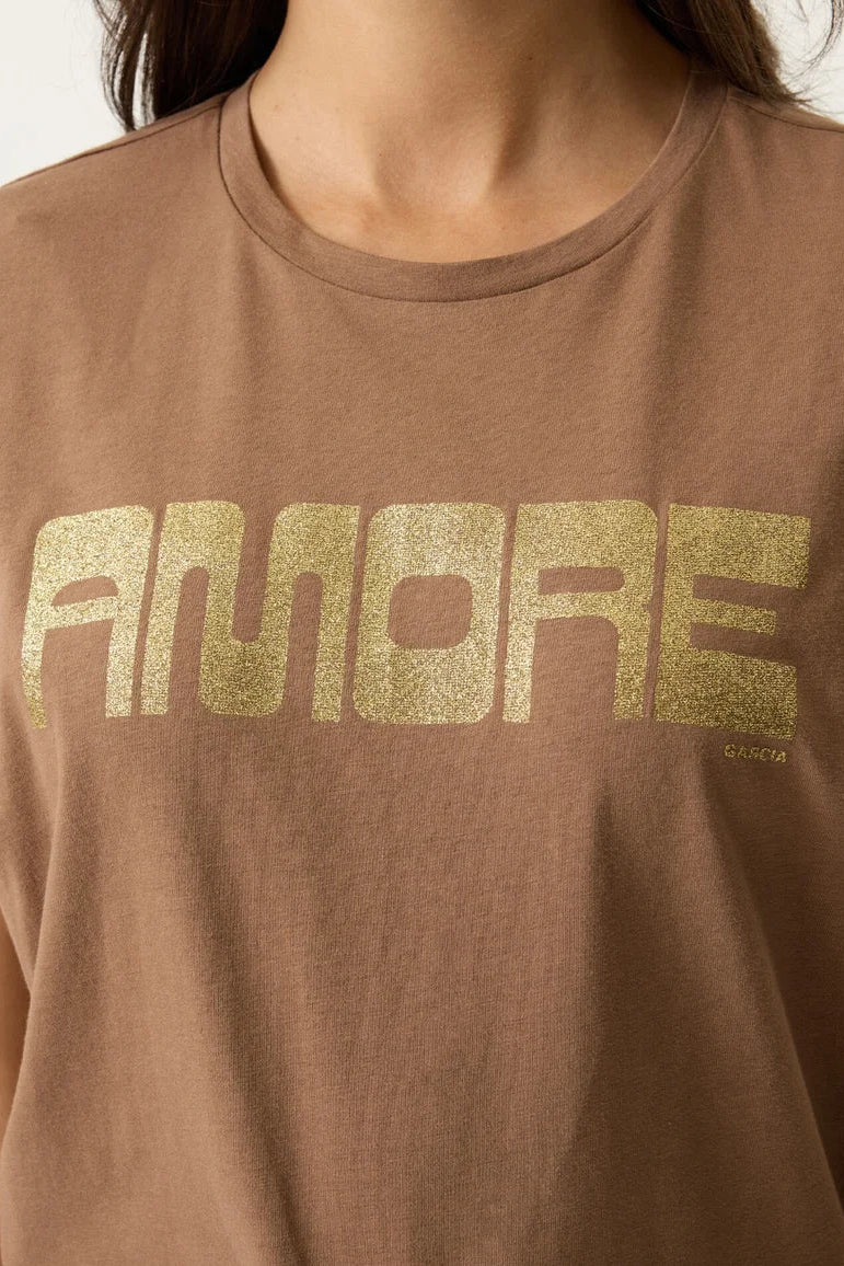A close-up of a person wearing a brown crewneck t-shirt with the word 'AMORE' printed across the chest in a textured gold glitter font.