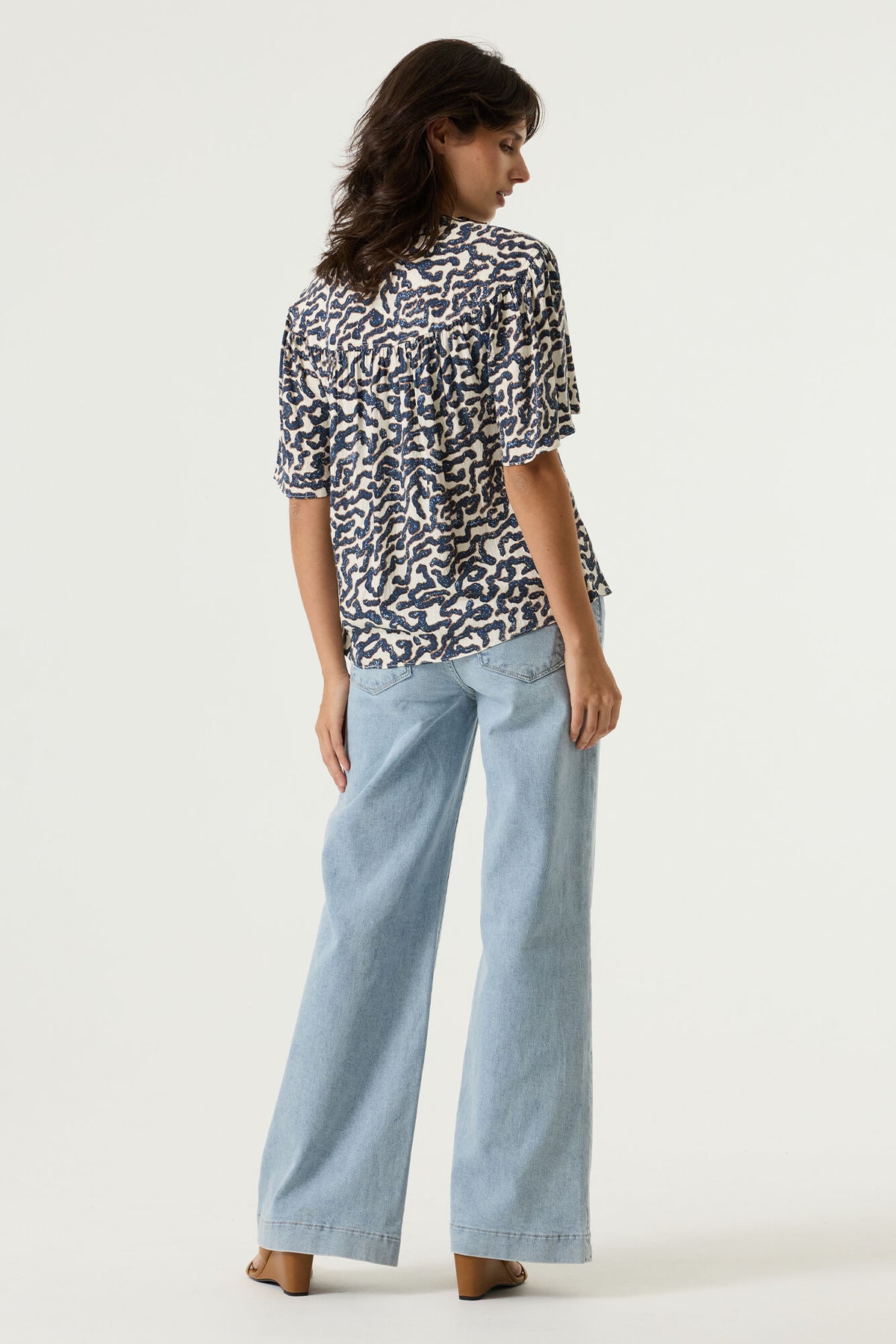 Woman shown from the back wearing a patterned shirt and light blue jeans on a white background