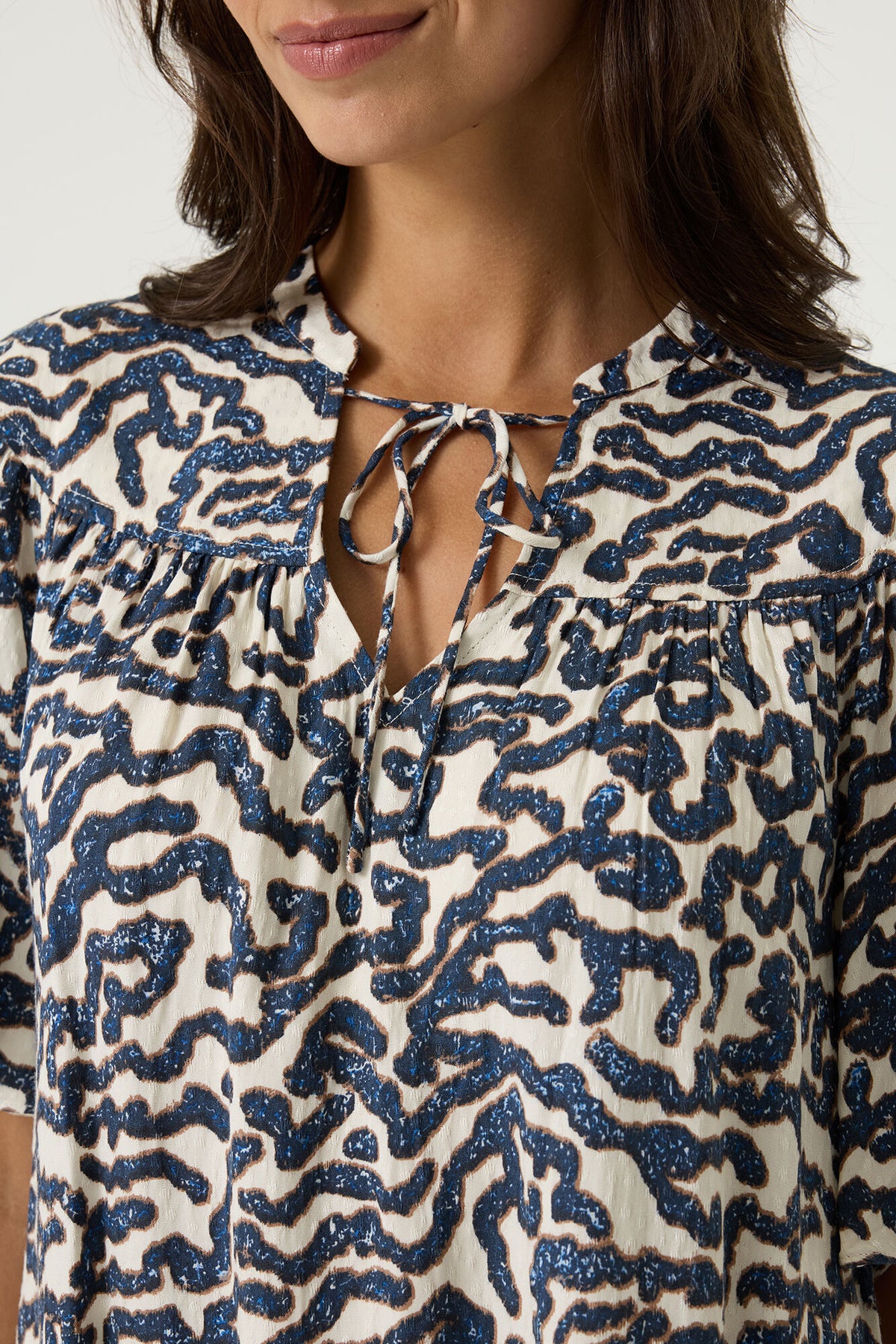 Close-up of a woman wearing a patterned blouse with blue and  white abstract design.