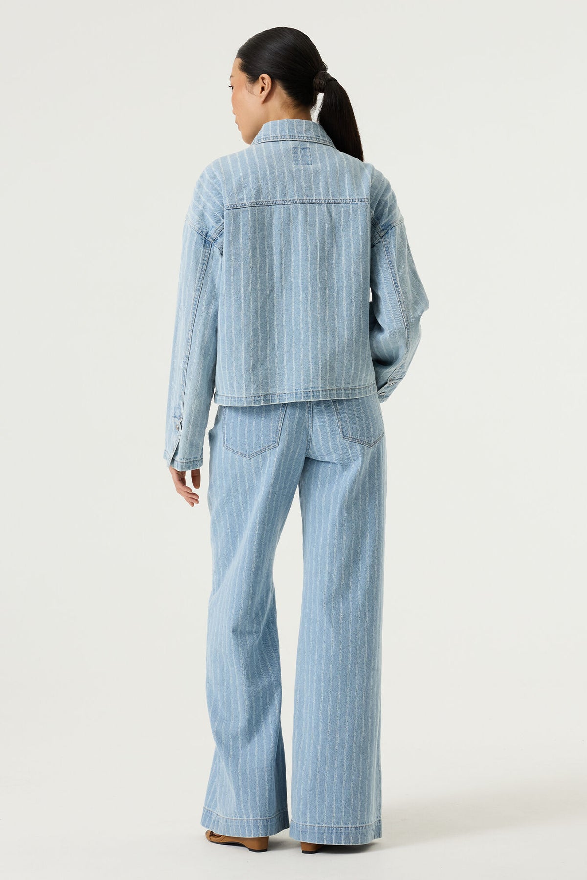Model shown from the back wearing a light blue striped denim jacket and matching wide leg pants on a white background
