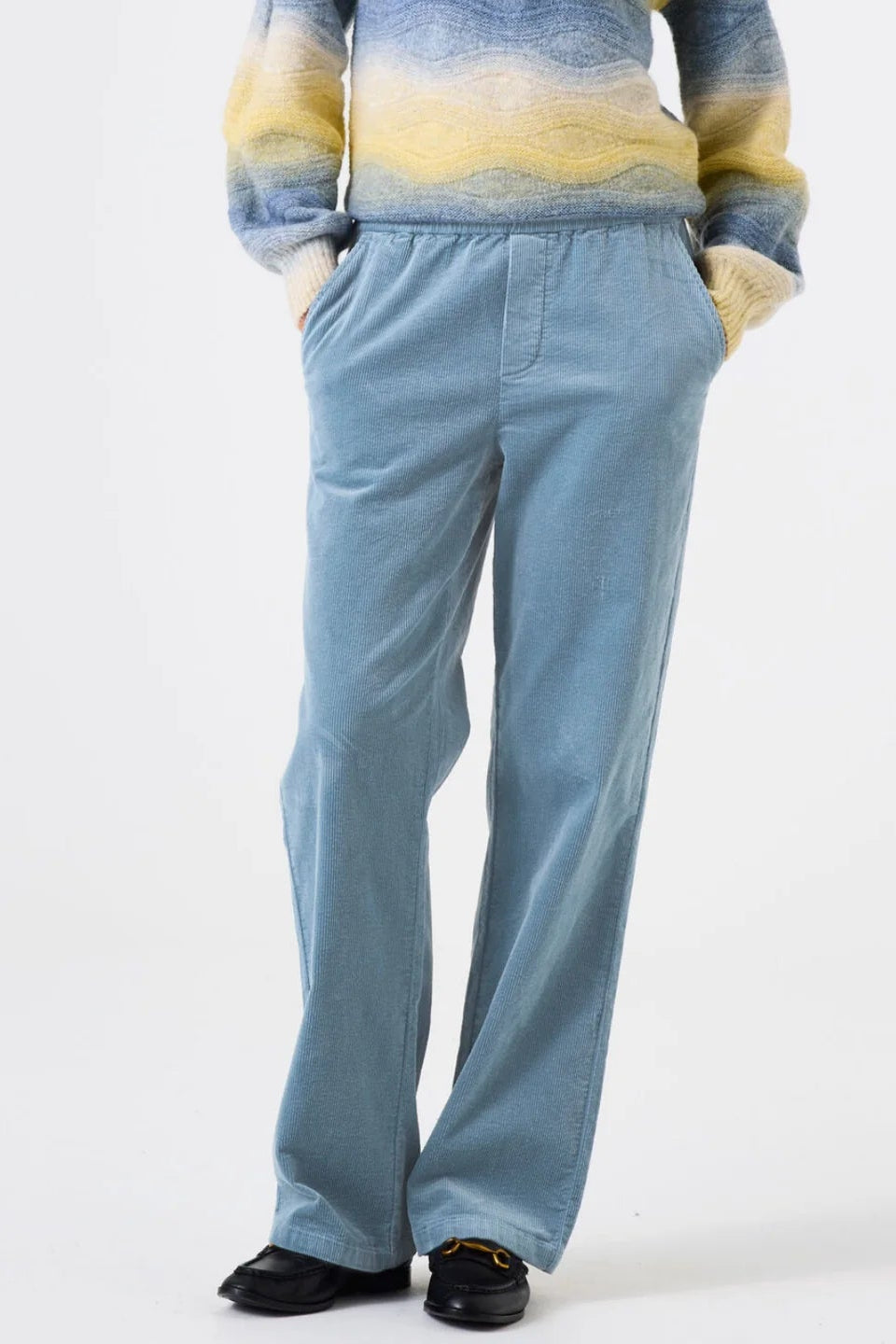 Person wearing light blue cord pants and a striped sweater on a white background