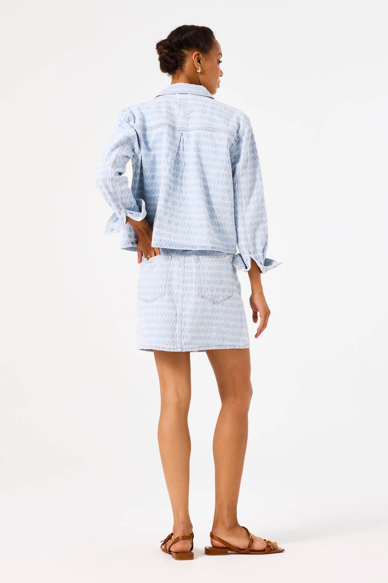 Woman wearing a light blue denim jacket and matching skirt on a white background
