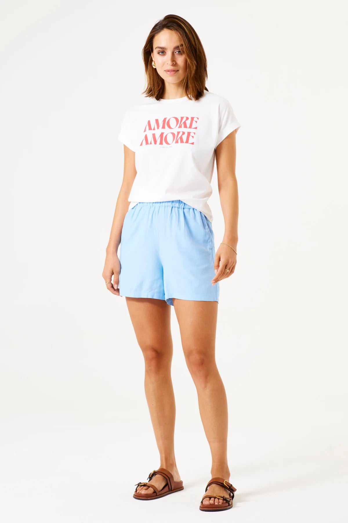 Woman wearing a white t-shirt with 'AMORE AMORE' text and light blue shorts on a white background