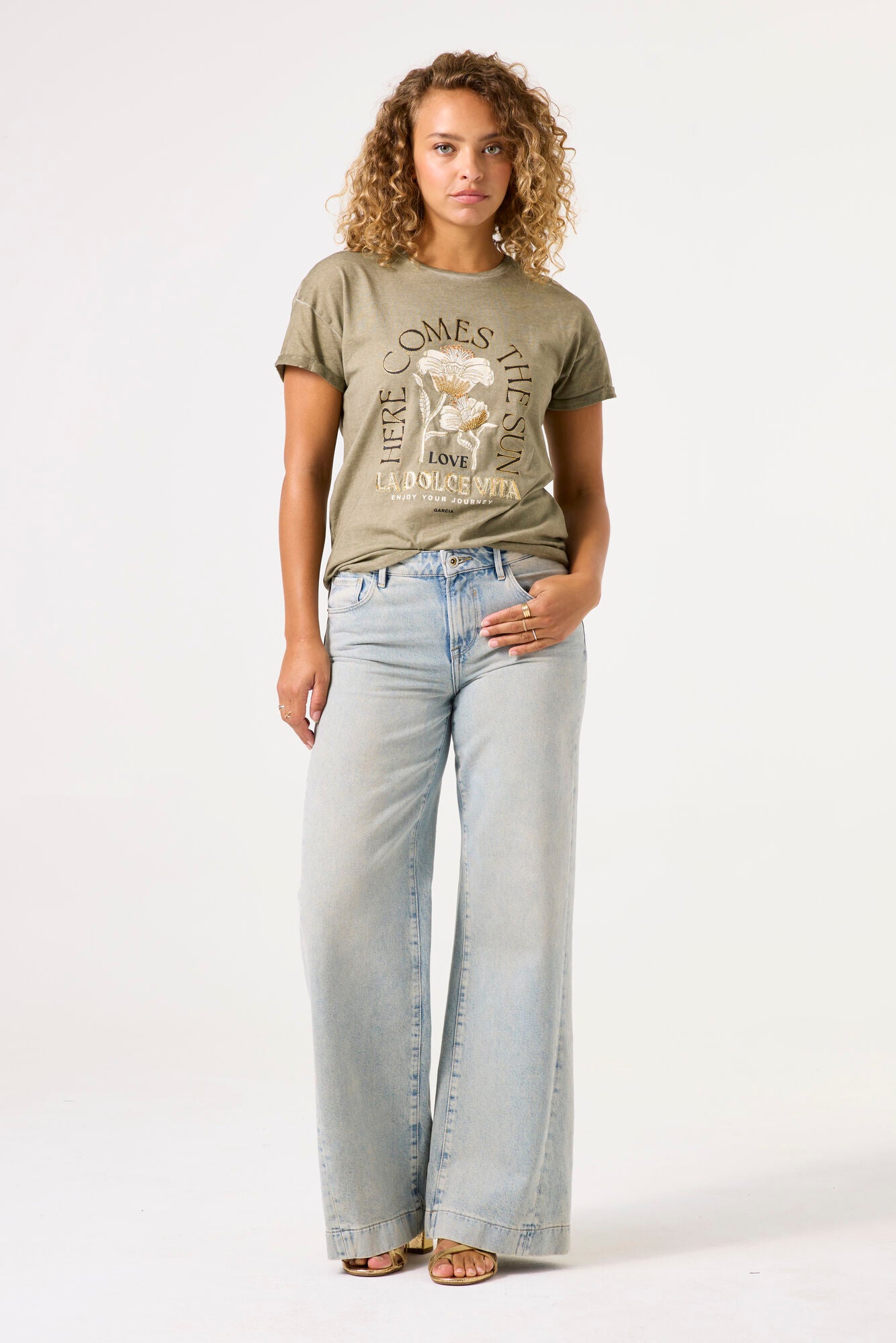 Model wearing here comes the sun graphic tee in olive from garcia with denim jeans on a white background. 