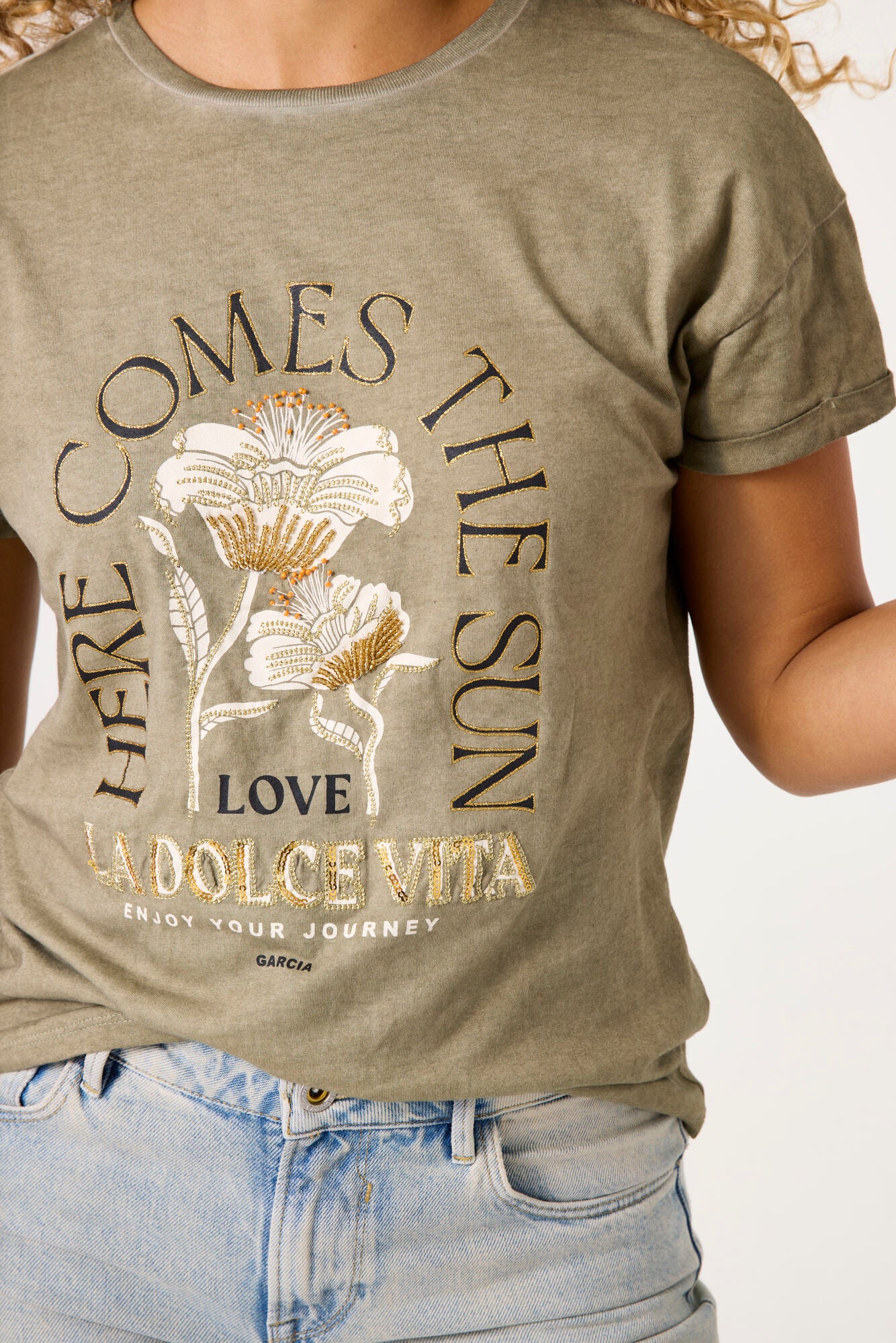 Model wearing here comes the sun graphic tee in olive from garcia with denim jeans on a white background. 