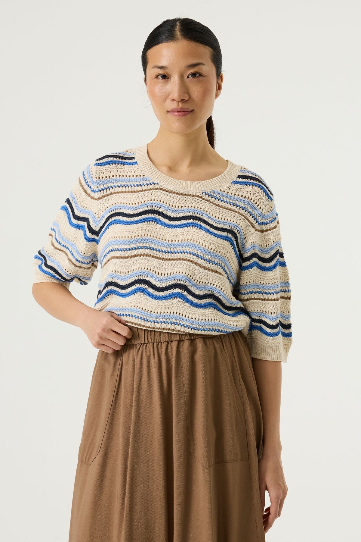 Woman wearing a patterned short sleeve sweater and brown skirt on a white background