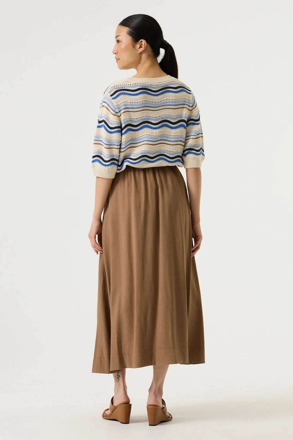 Woman shown from the back wearing a striped sweater and brown skirt on a white background