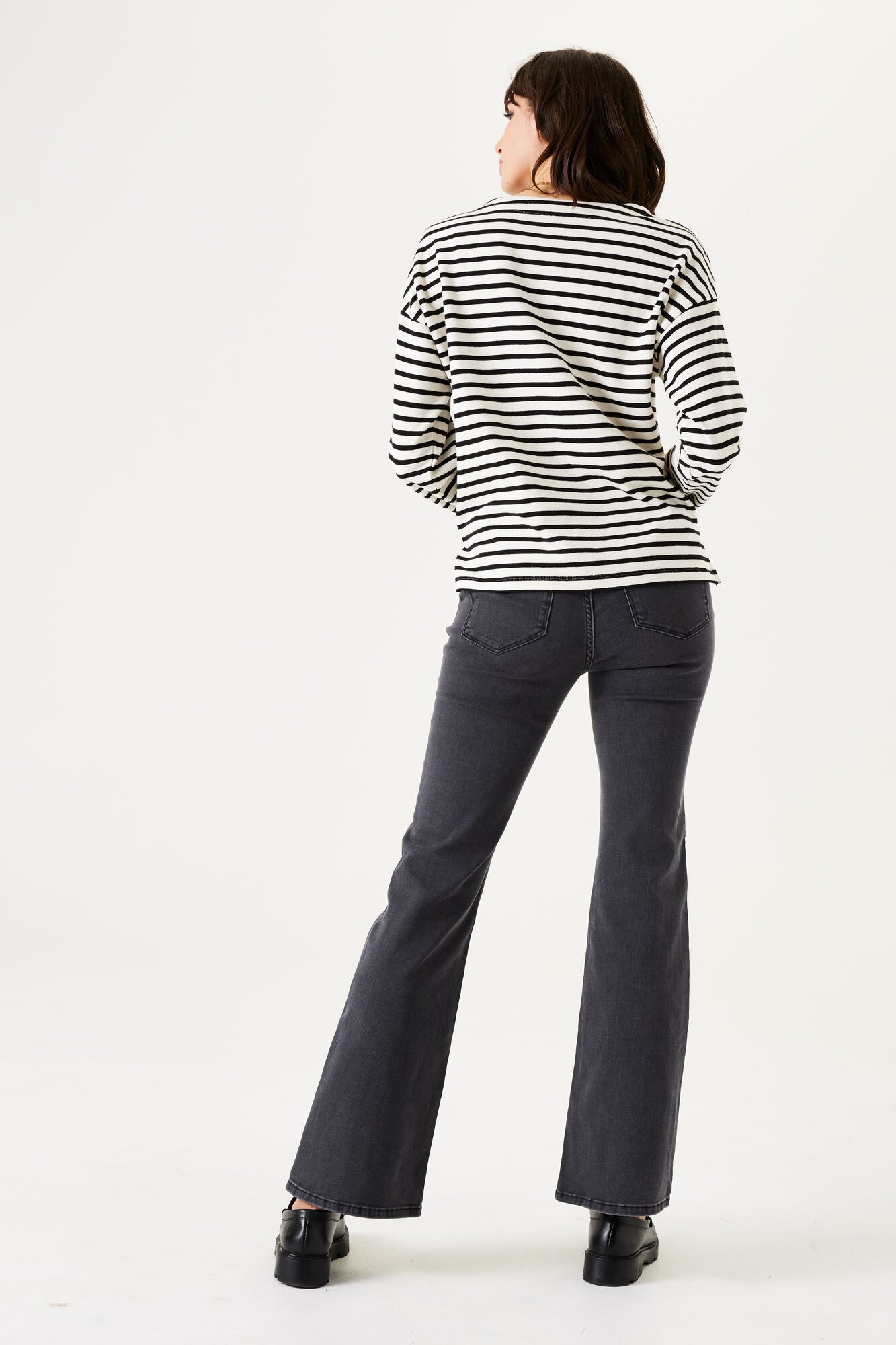 Woman wearing a black and white striped sweater and dark pants on a white background