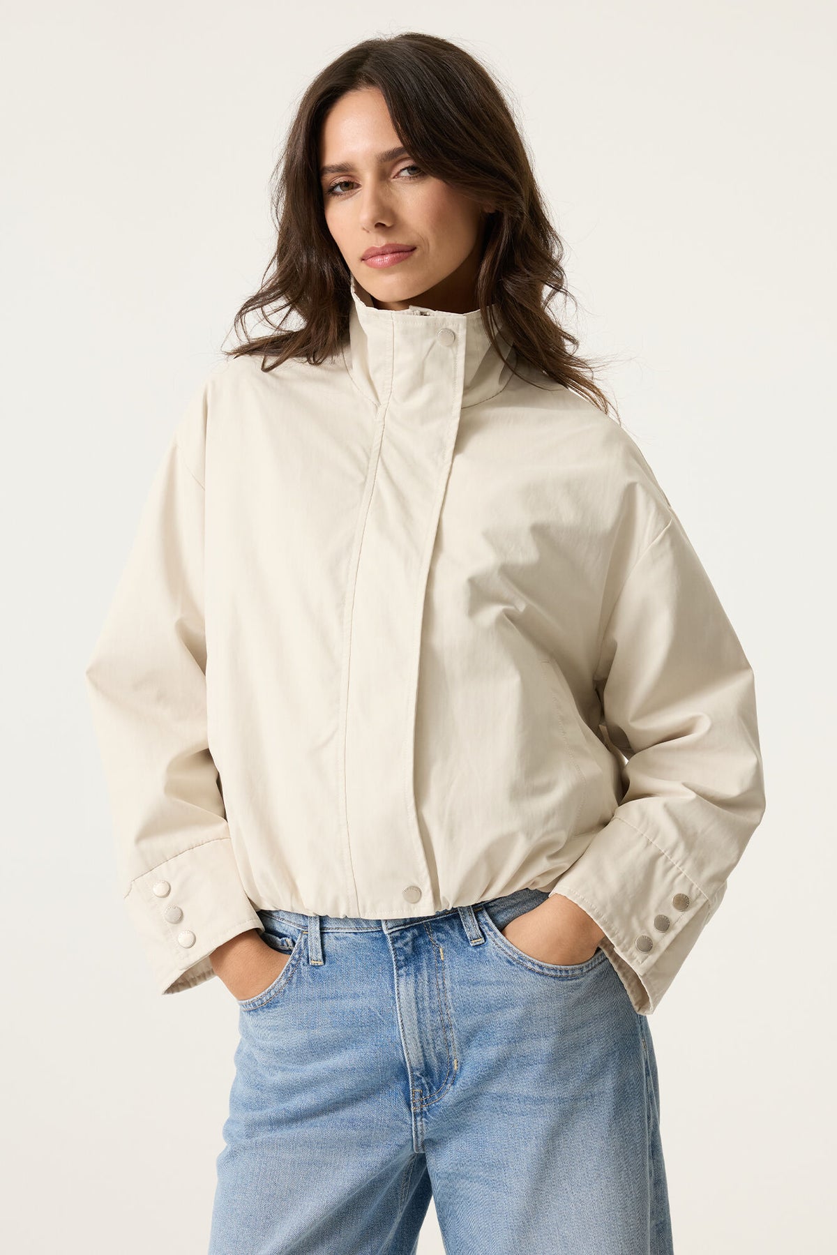 Woman wearing a off white cropped jacket and blue jeans on a white background