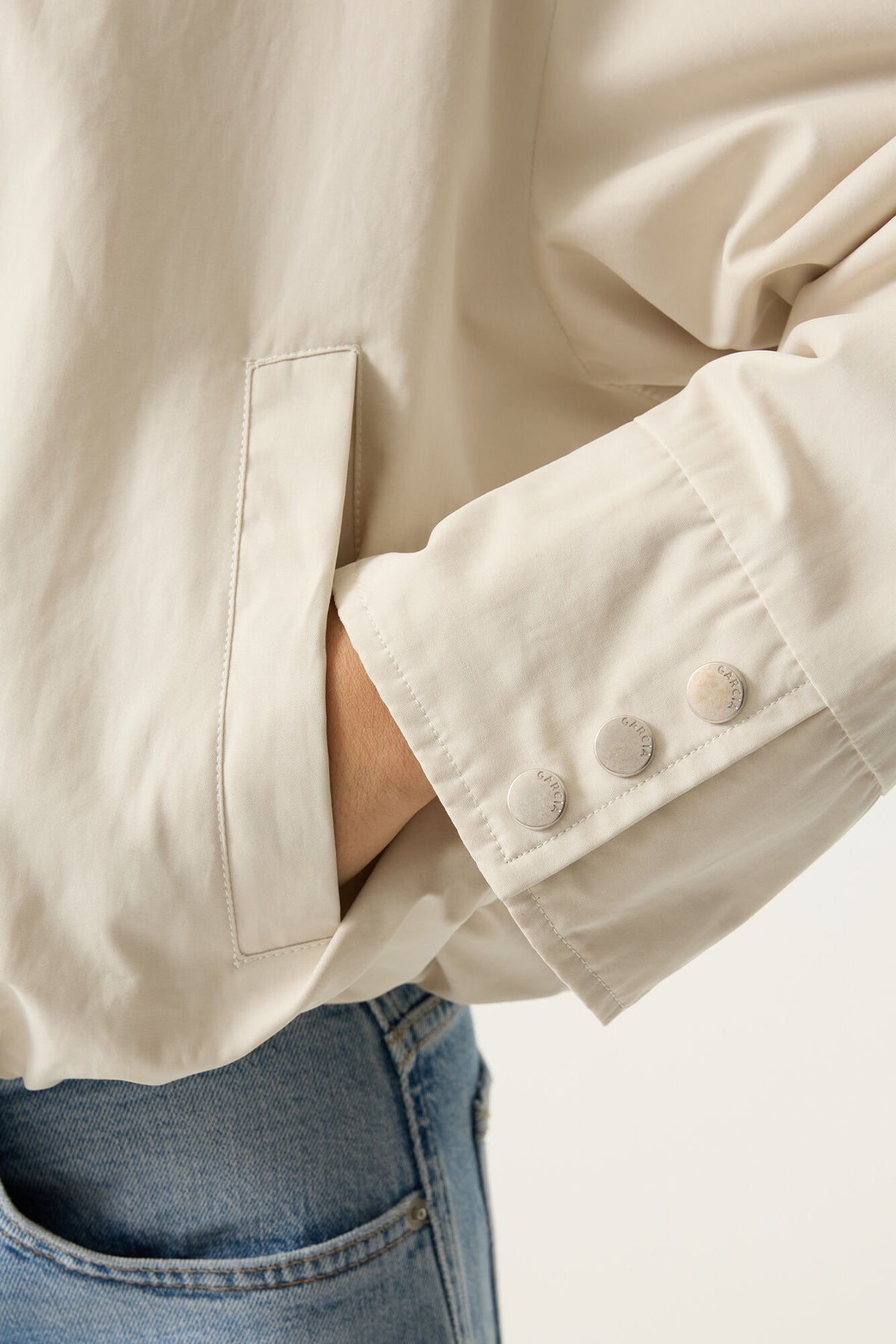Close-up of a beige jacket with dome sleeve detail and blue jeans on a light background