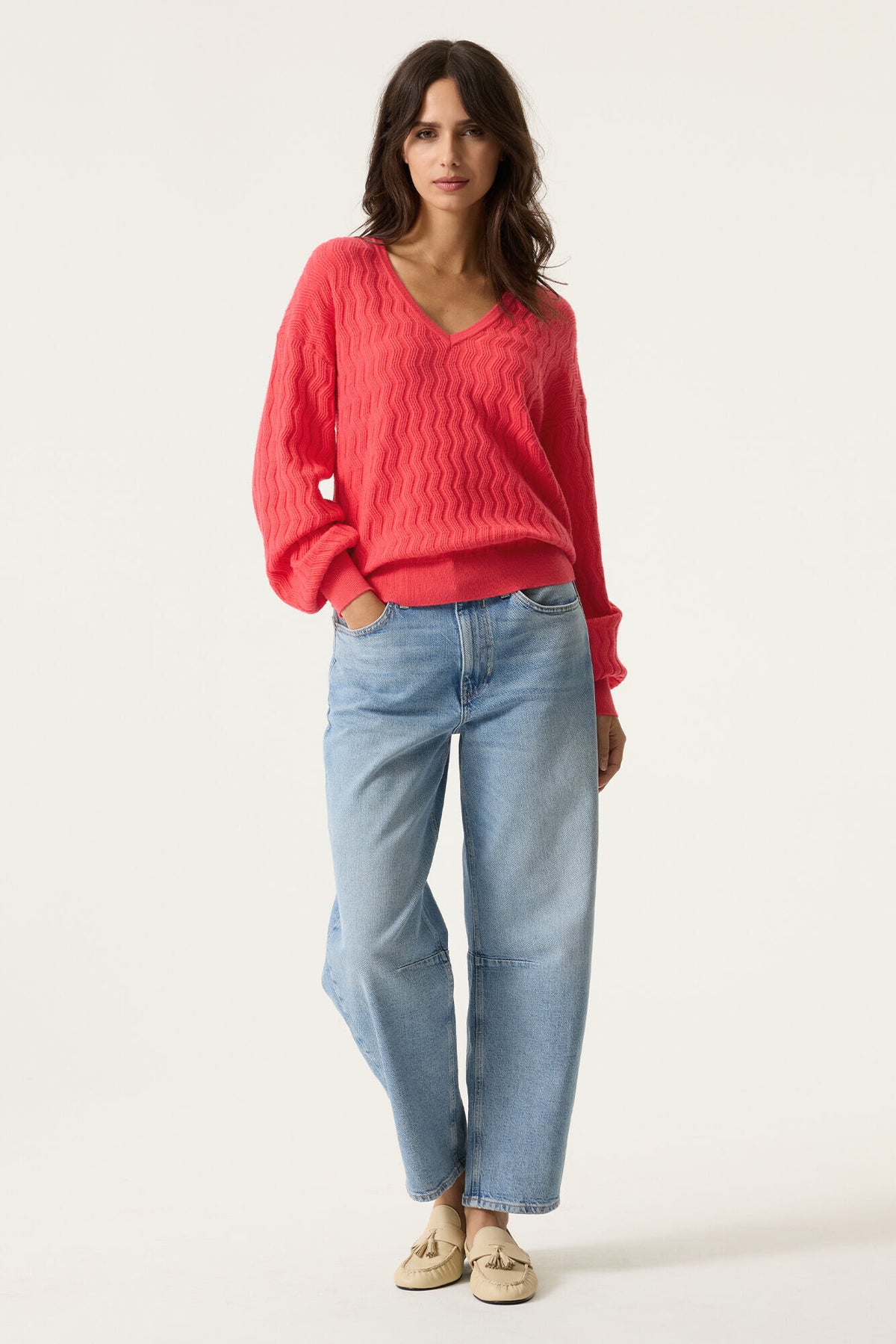 Woman wearing a  v neck pink sweater and light blue jeans on a white background