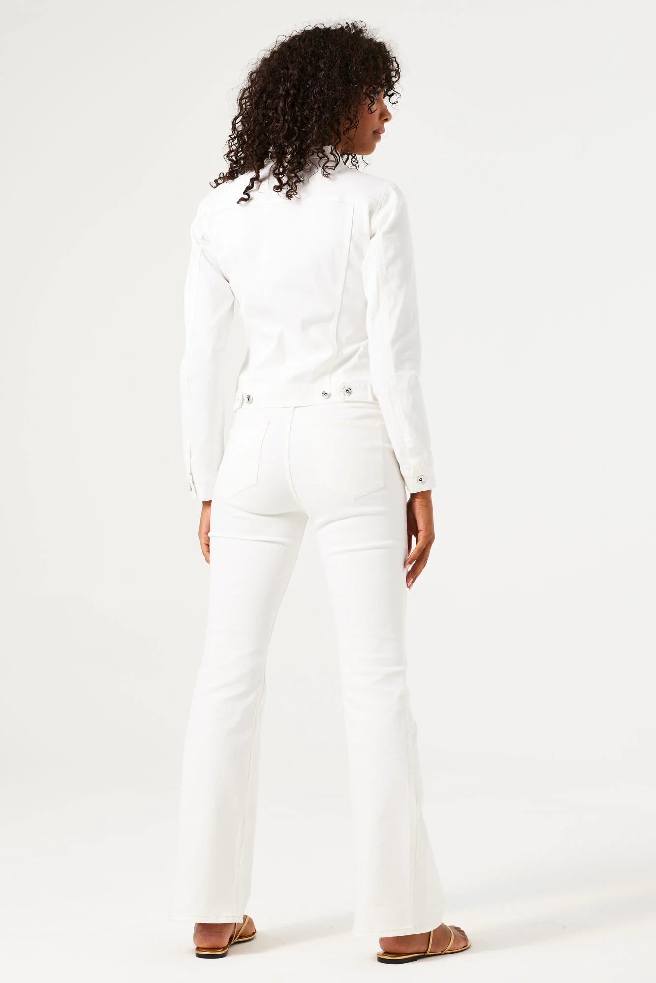 Model wearing a white cropped denim jacket and jeans with sandals on a white background