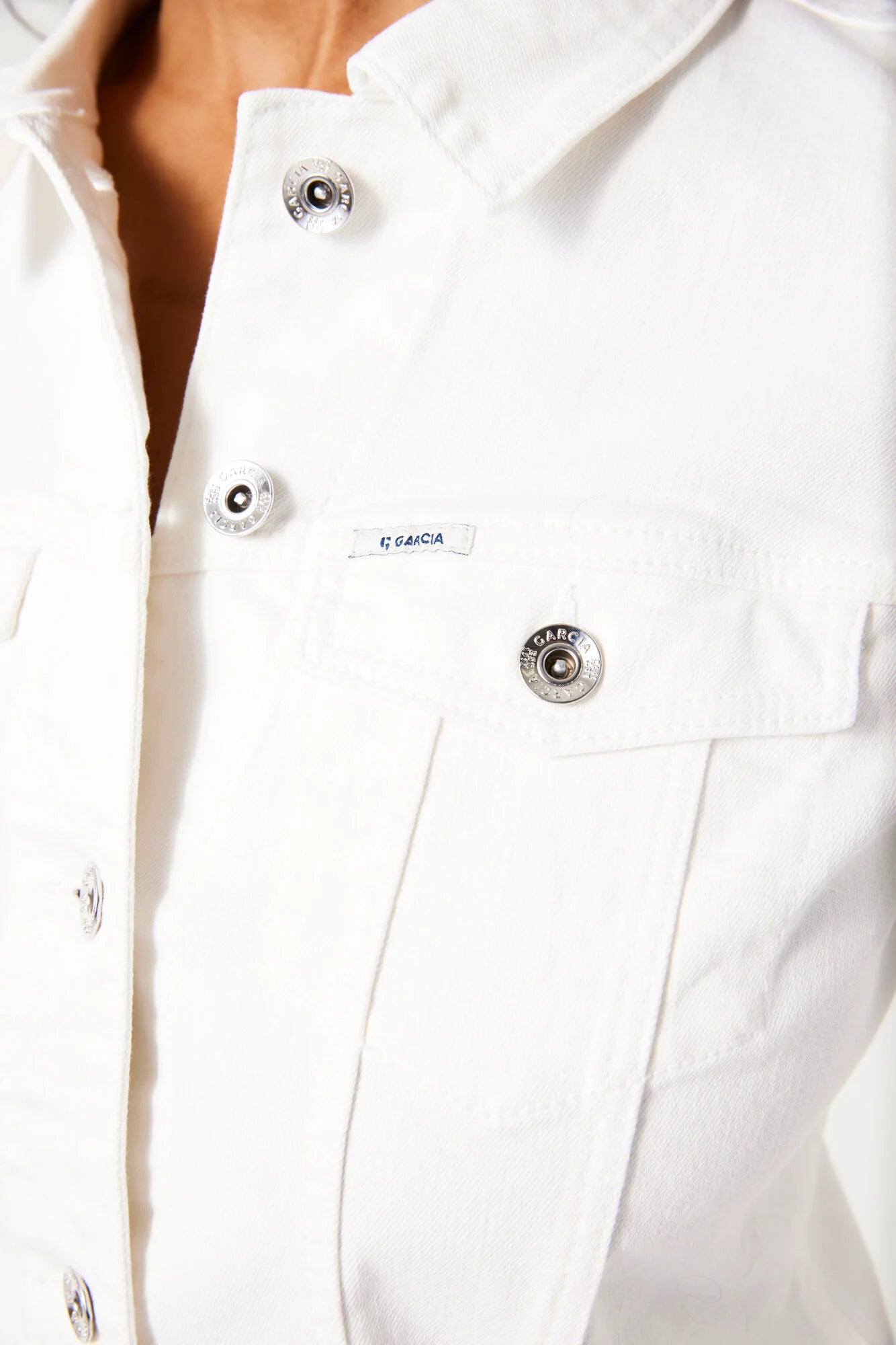 Close-up of a white denim jacket with buttons and a visible Garcia brand logo.