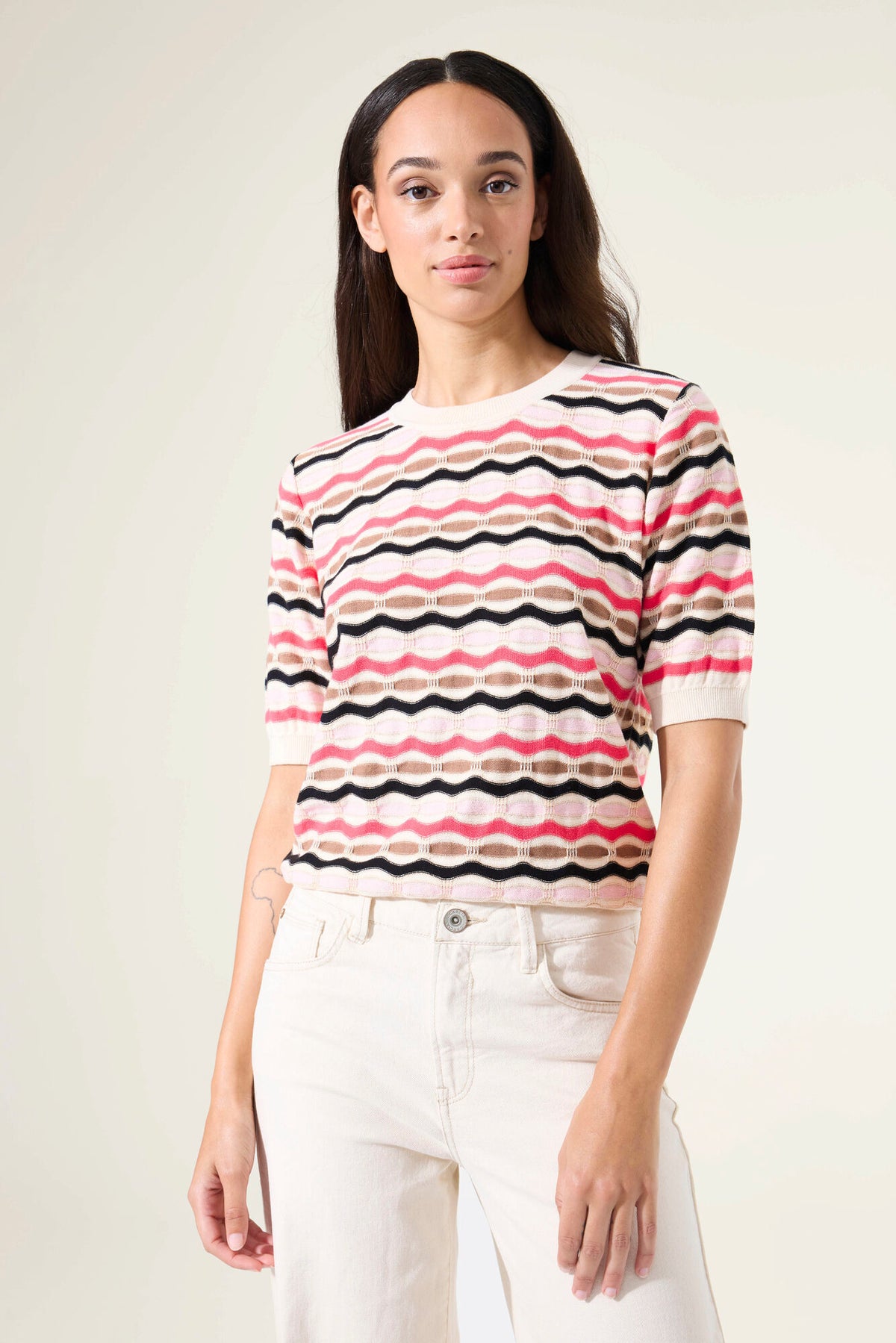Woman wearing a short sleeve striped sweater and white pants against a plain background