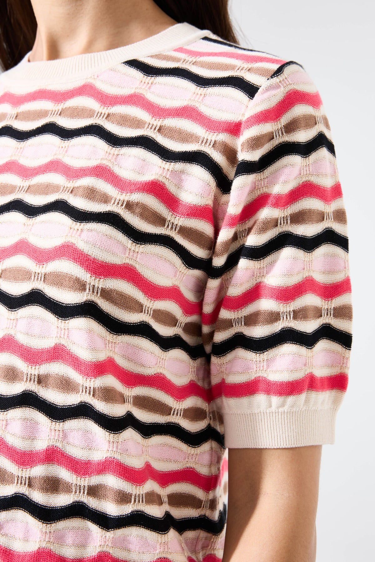 Woman up close wearing a short sleeve striped sweater against a plain background