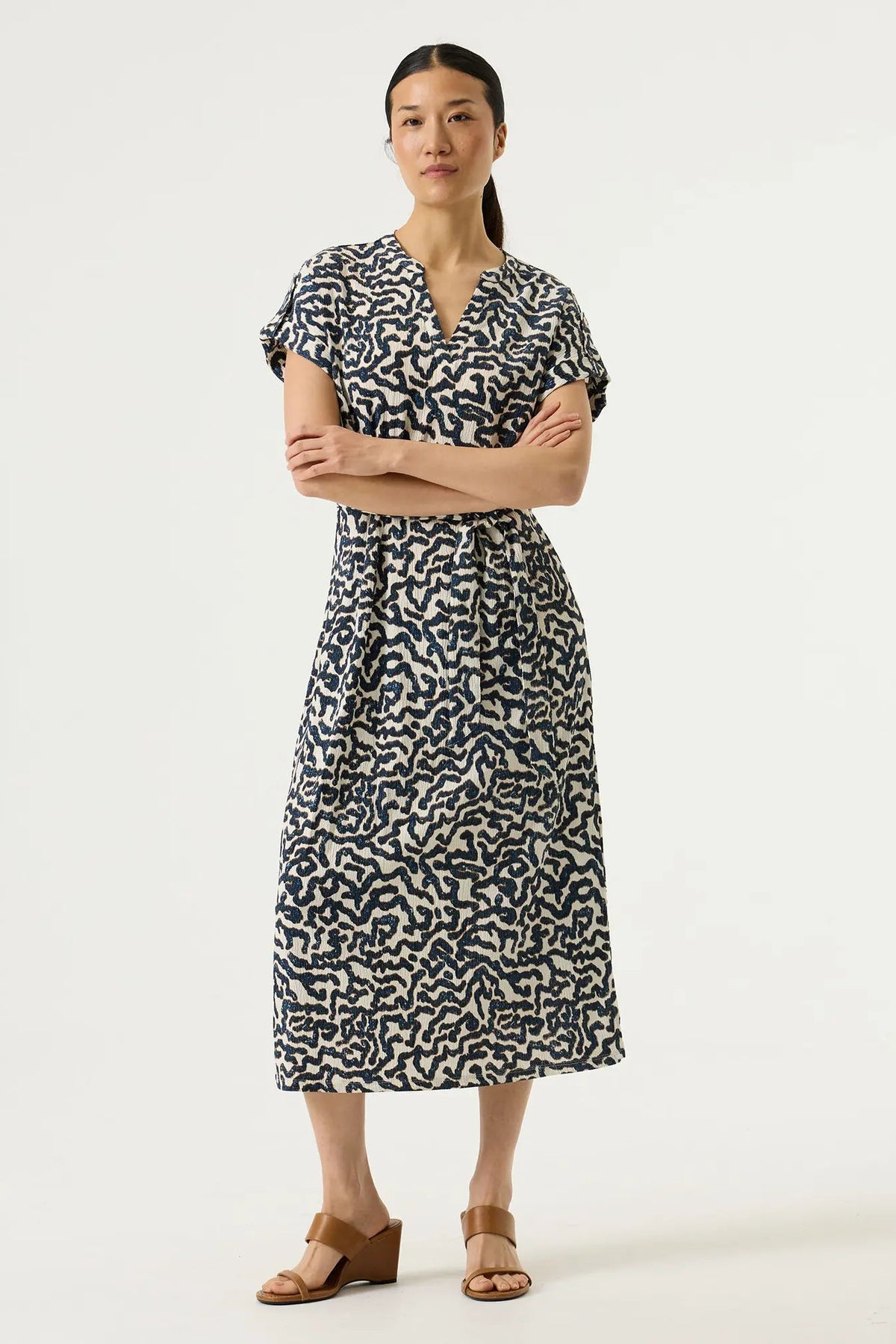 Woman shown from the back wearing a textured cream-coloured dress with a dark navy blue abstract wavy pattern and a matching tie belt at the waist.